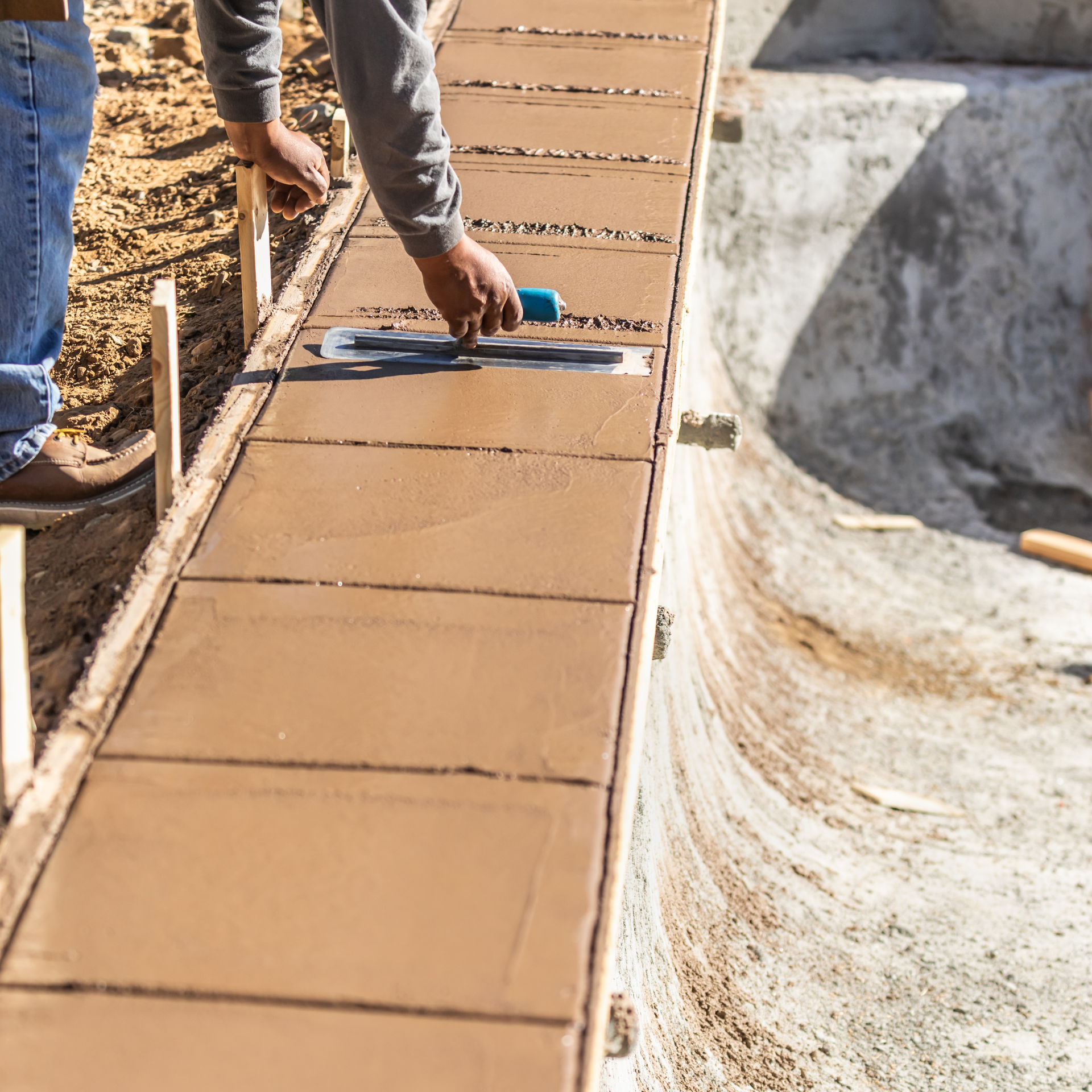 A man is using a trowel to spread concrete on a sidewalk