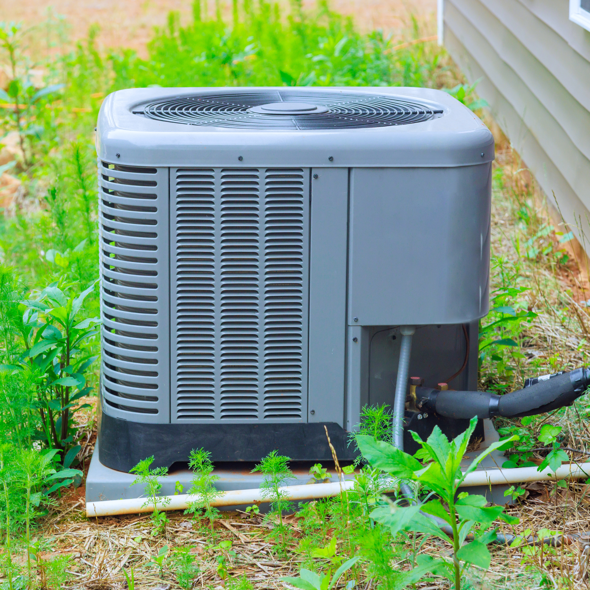An air conditioner is sitting outside of a house in the grass.
