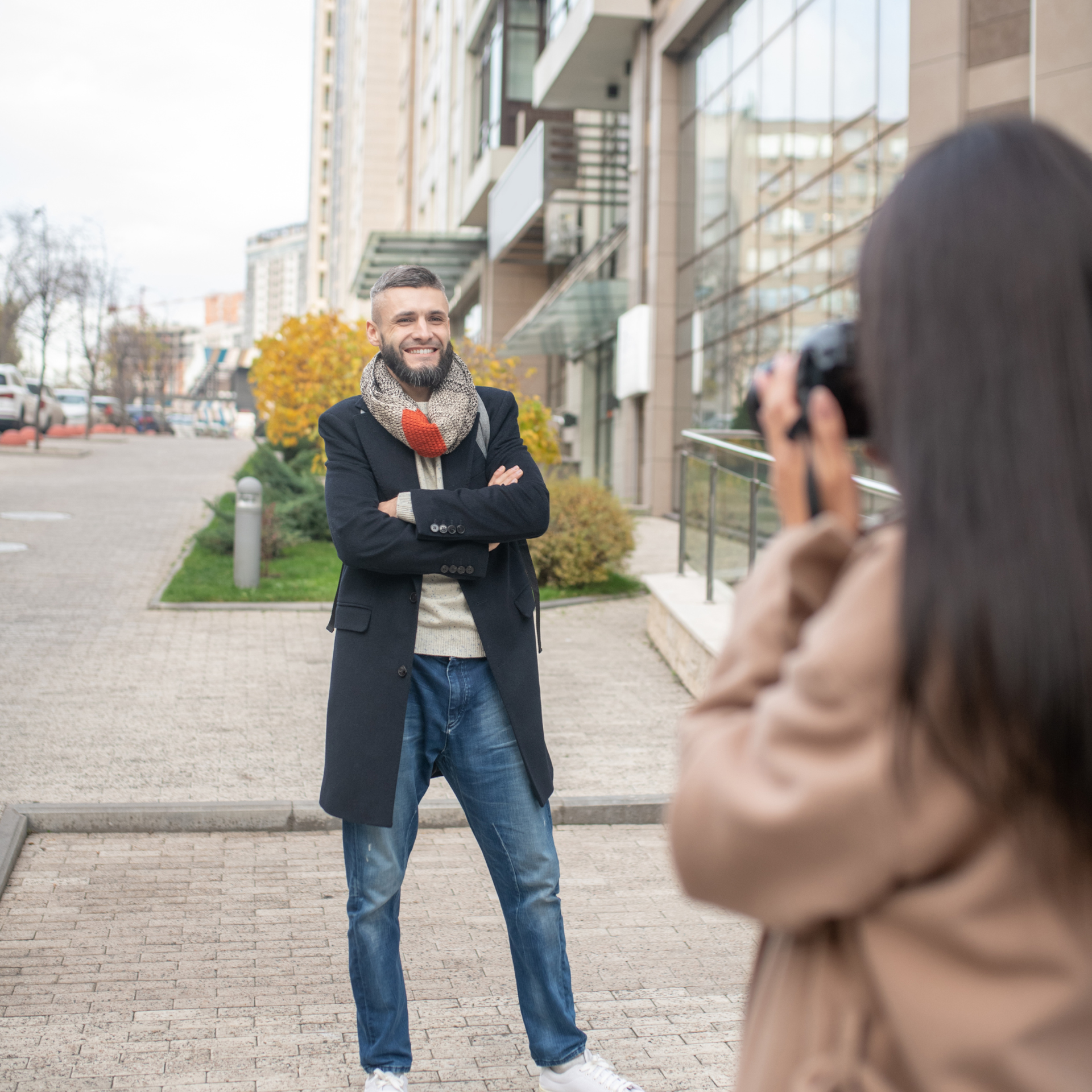 A woman is taking a picture of a man with his arms crossed