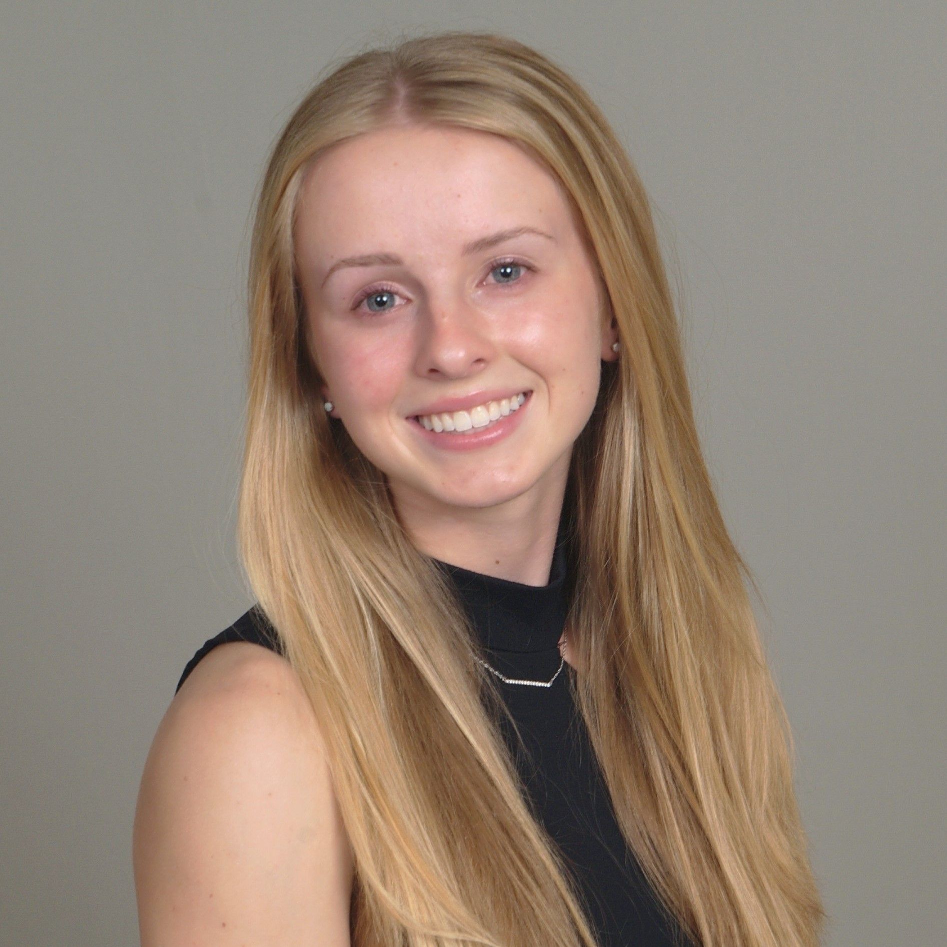 A woman with long blonde hair is wearing a black top and smiling.