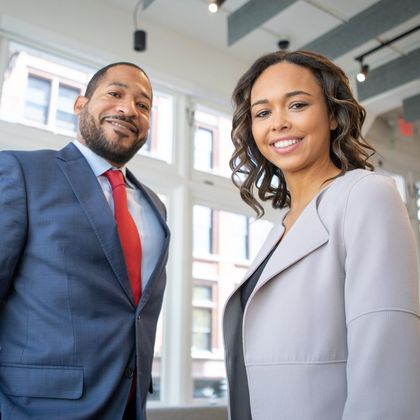 A man in a suit and tie stands next to a woman in a grey jacket