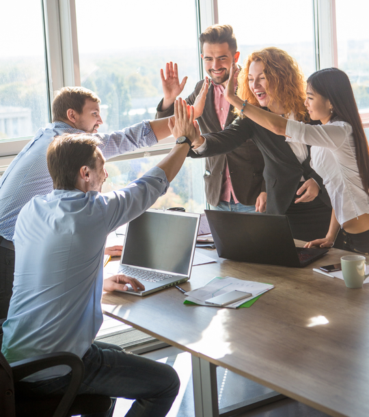 A group of people are giving each other a high five in an office.