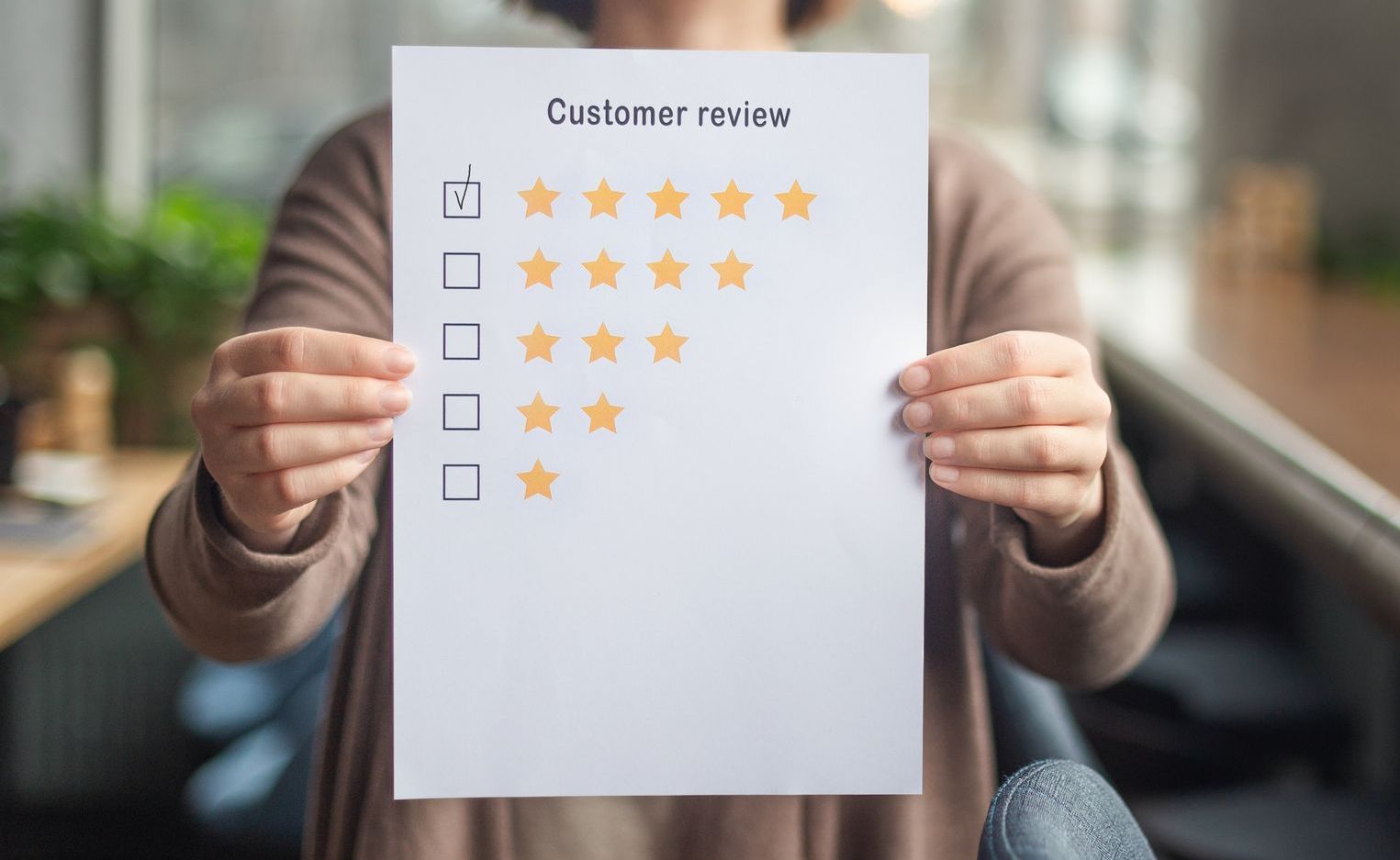 A woman is holding a piece of paper with a customer review on it.