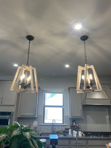 Two light fixtures hang above a kitchen island with cabinets and a window. Two light fixtures hang above a kitchen island with cabinets and a window.