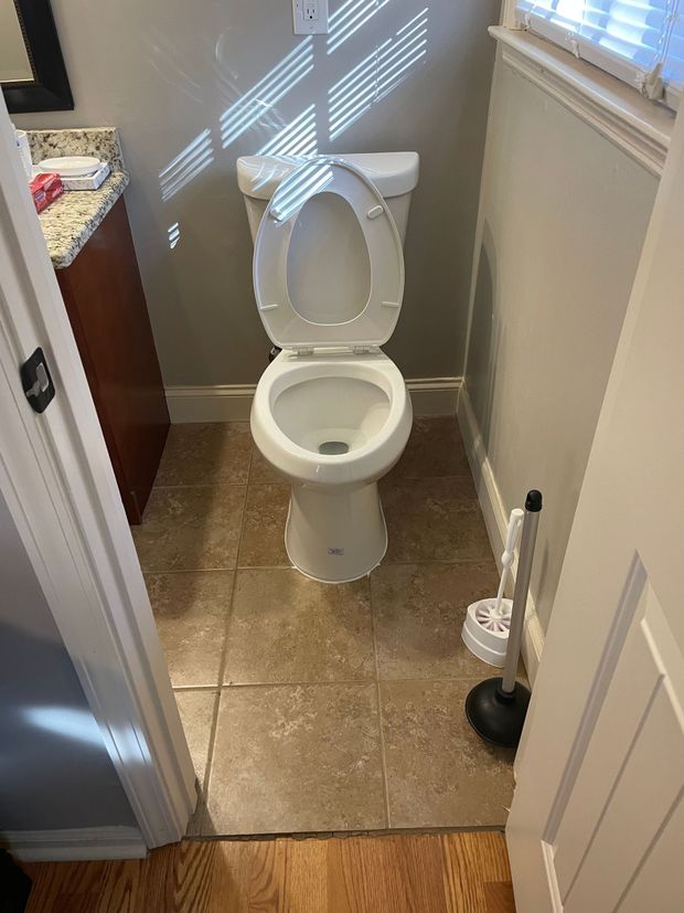 Bathroom with a white toilet, tile floor, and a toilet brush. Bathroom with a white toilet, tile floor, and a toilet brush.
