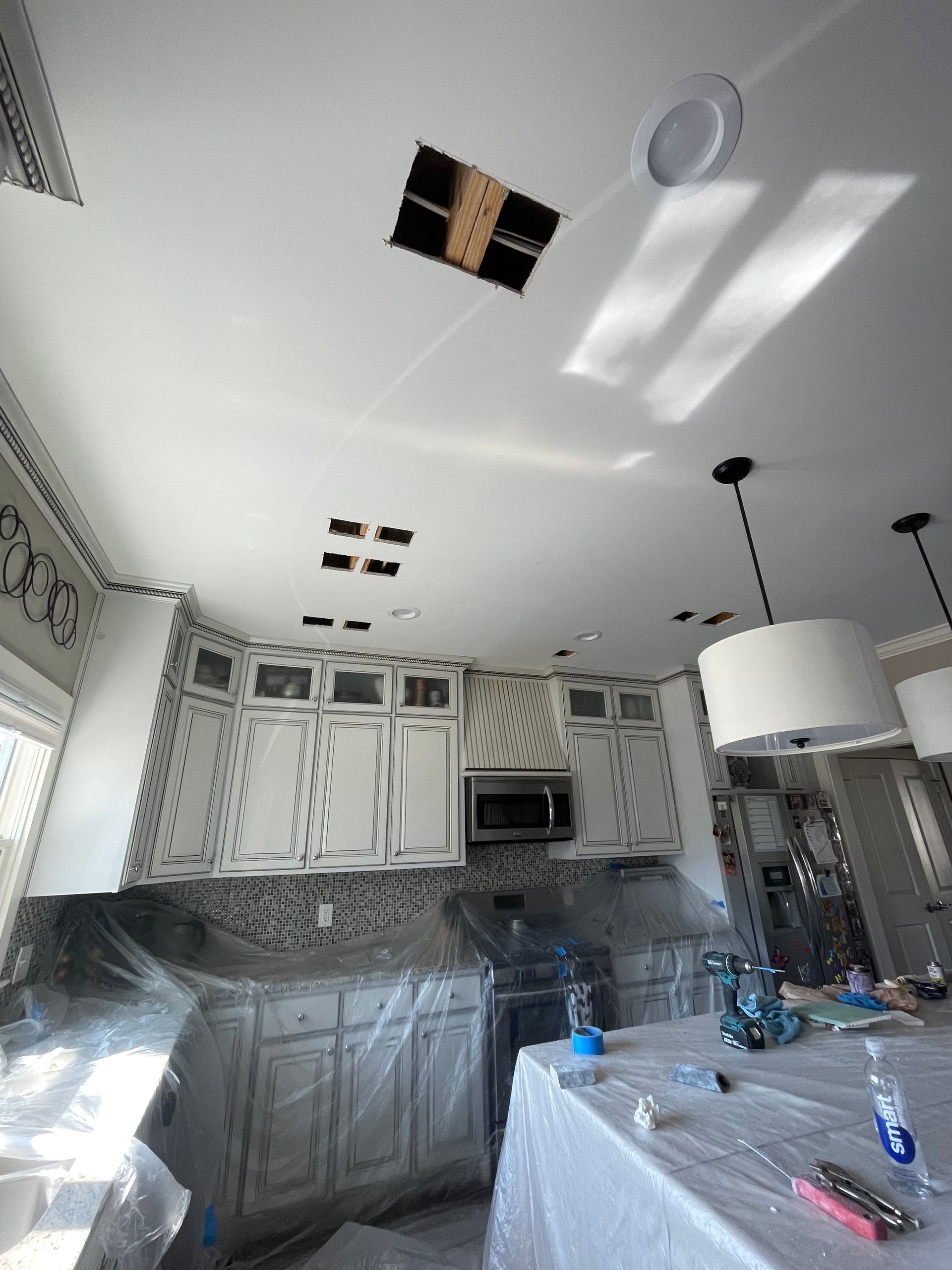 Kitchen with white cabinets, holes in the ceiling for lights, and protective plastic covering surfaces. Kitchen with white cabinets, holes in the ceiling for lights, and protective plastic covering surfaces.