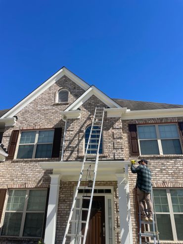 Person on ladder, working on the front of a brick house. Blue sky overhead. Person on ladder, working on the front of a brick house. Blue sky overhead.