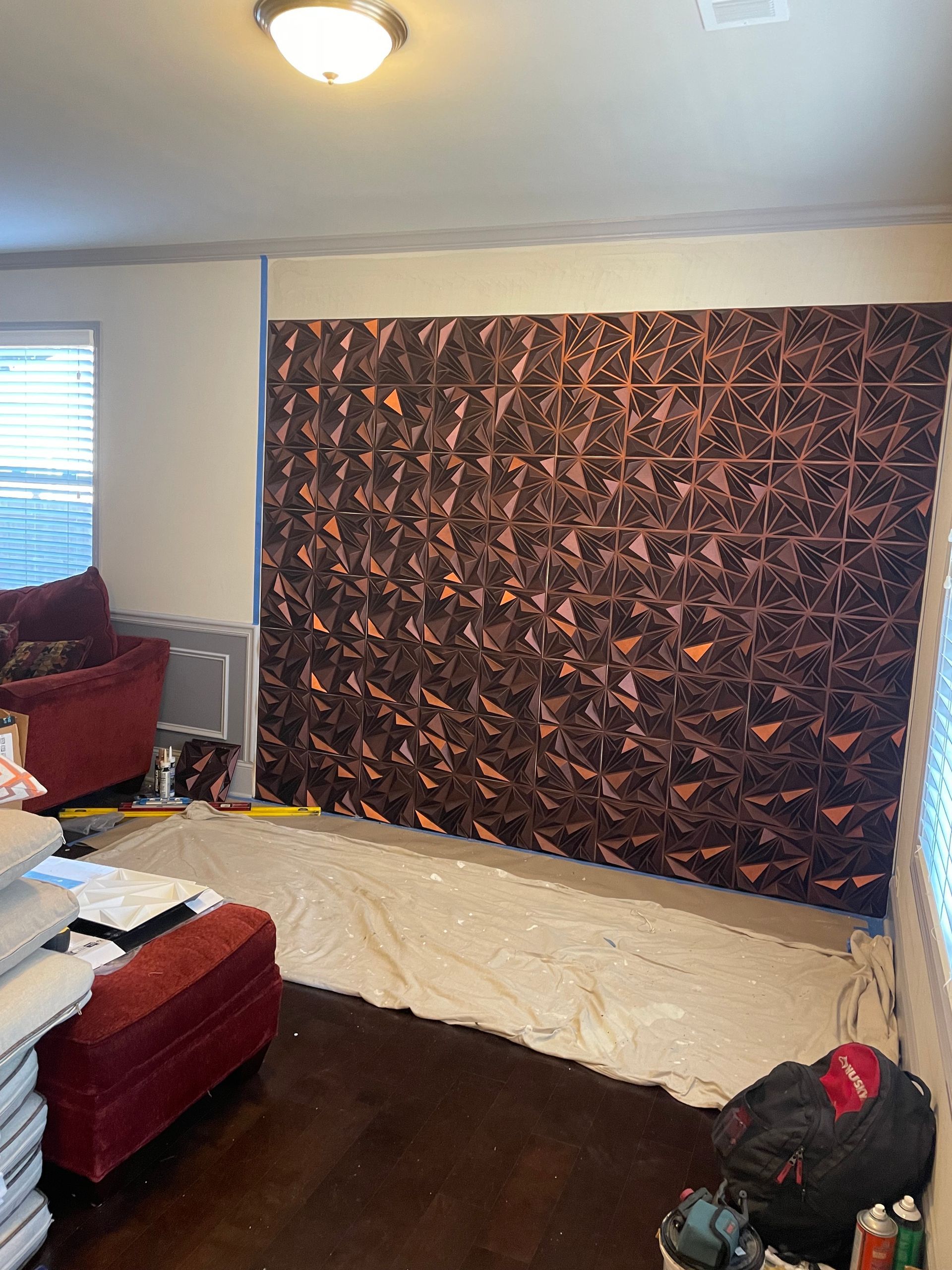 Living room with copper-colored wall decor, red furniture, and protective sheet on the floor. Living room with copper-colored wall decor, red furniture, and protective sheet on the floor.
