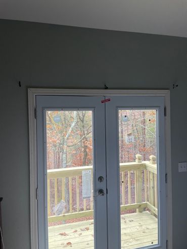 Exterior double doors with white trim and view of a wooden deck and trees. Exterior double doors with white trim and view of a wooden deck and trees.