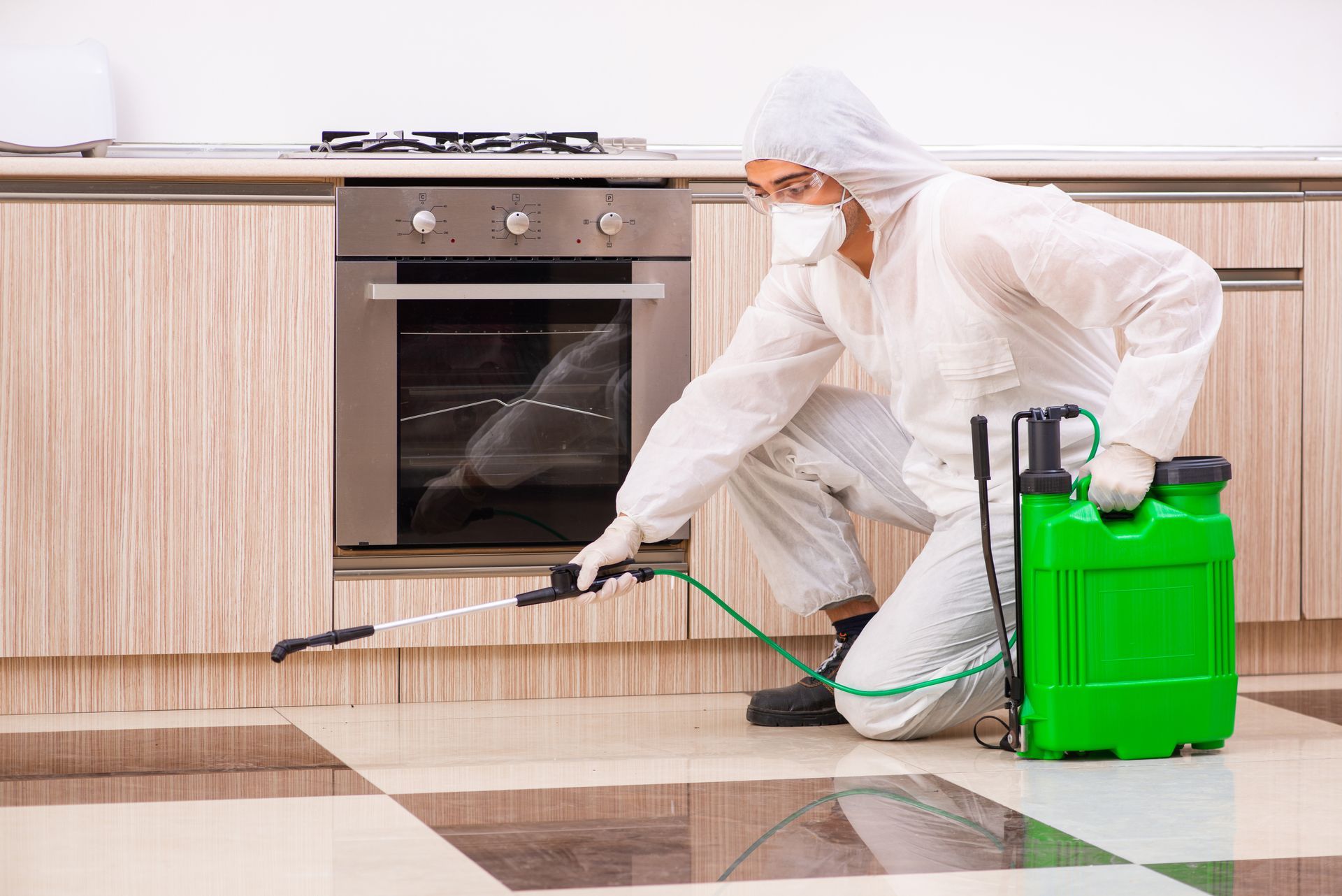 Cleaner in white protective suit spraying disinfectant on a kitchen floor with a green backpack sprayer Cleaner in white protective suit spraying disinfectant on a kitchen floor with a green backpack sprayer