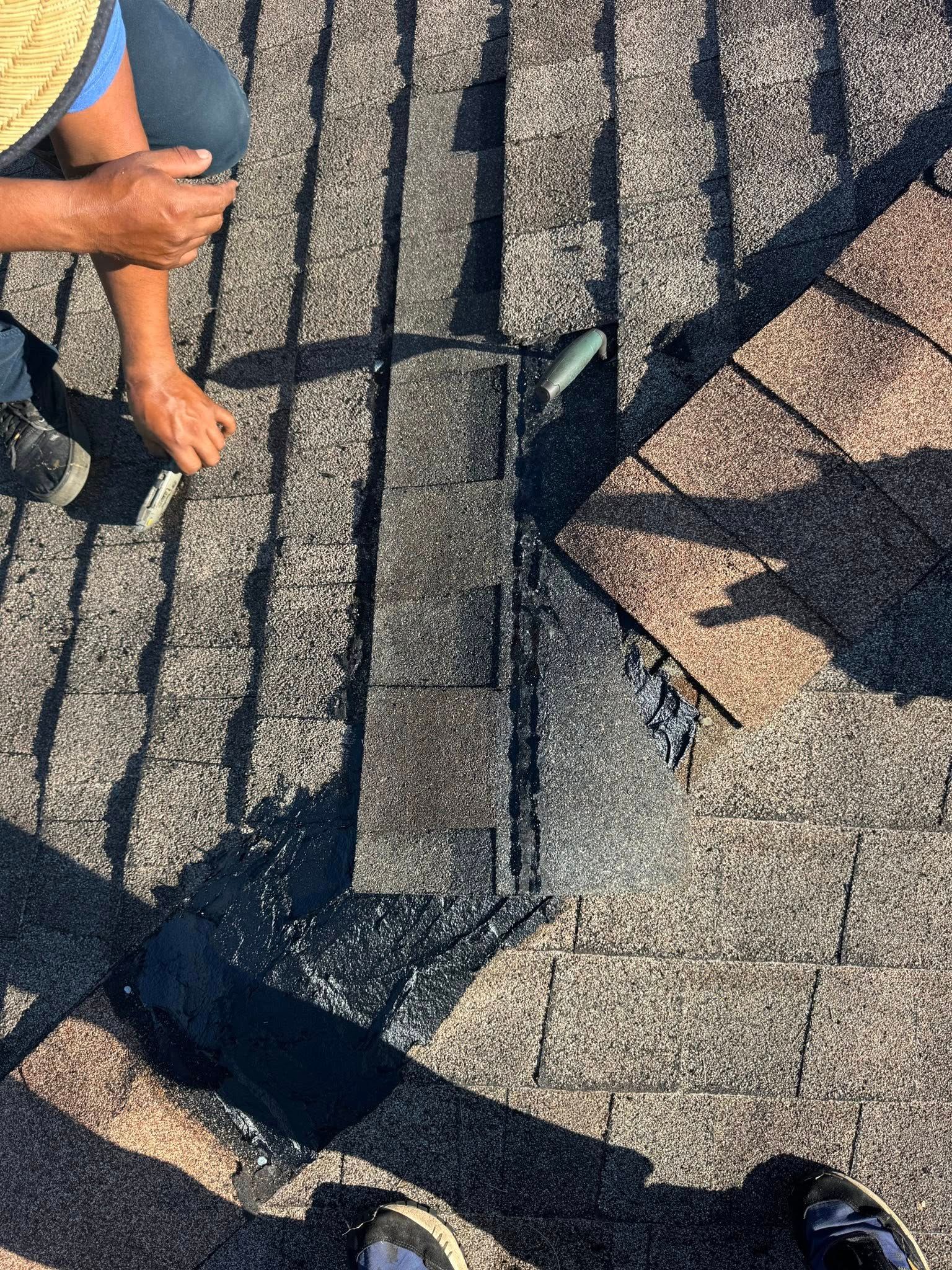 Person repairing roof shingles, replacing a damaged section.