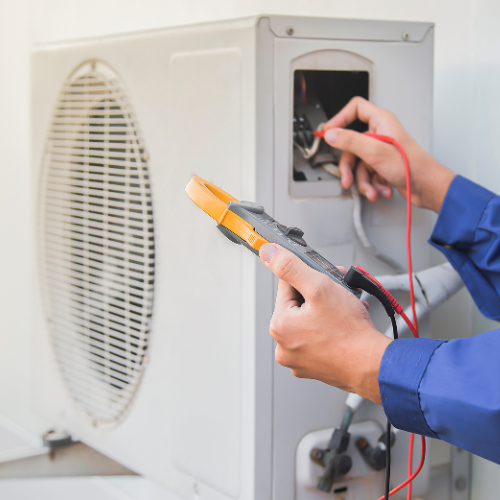 A person is holding a pair of pliers in front of an air conditioner.