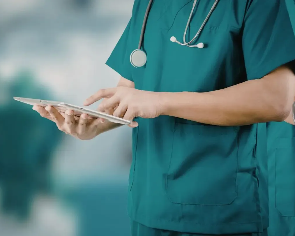 Doctor in teal scrubs with stethoscope, using a tablet.
