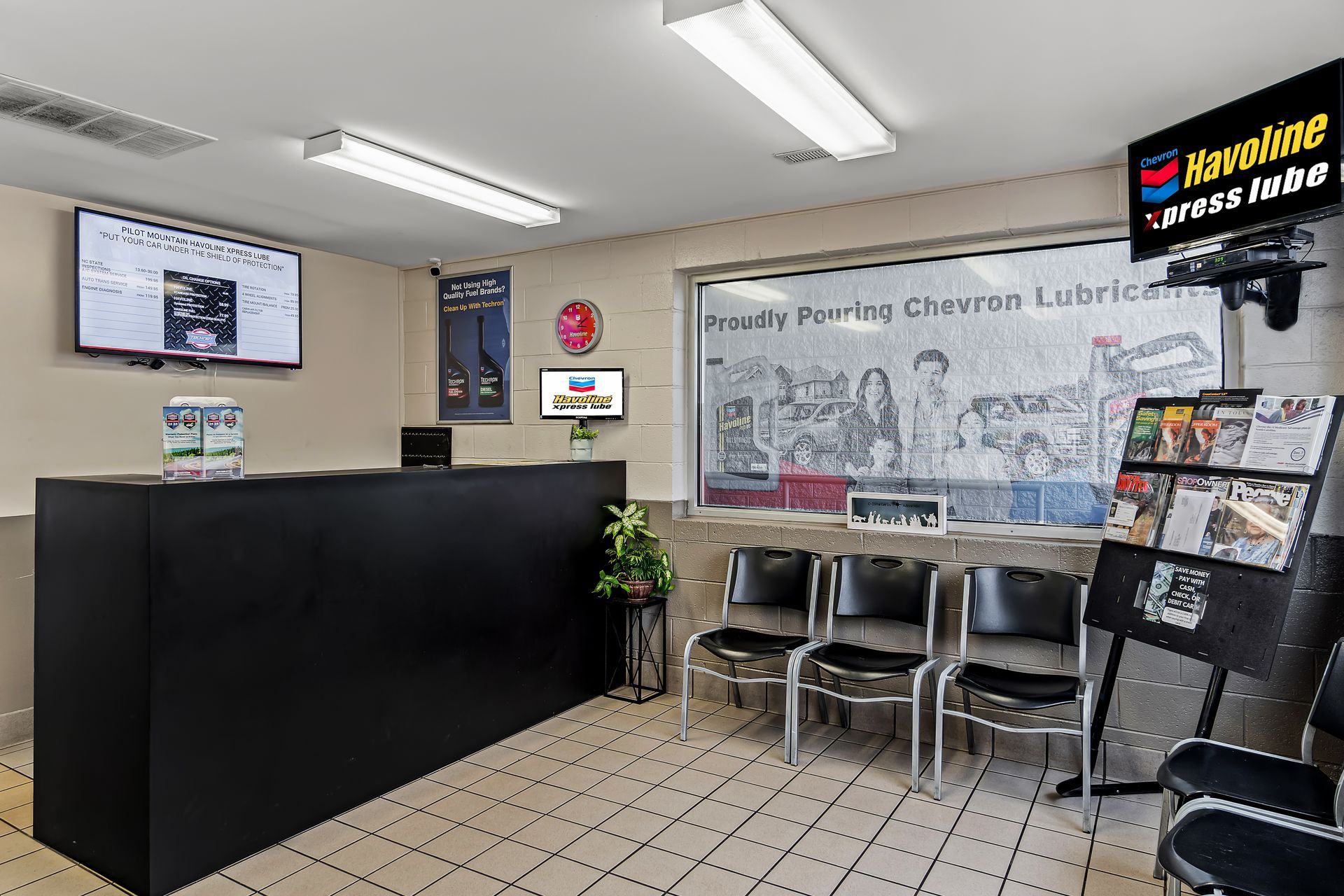Interior of a library check-in area with black counter, chairs, bookshelves, and informational signs.