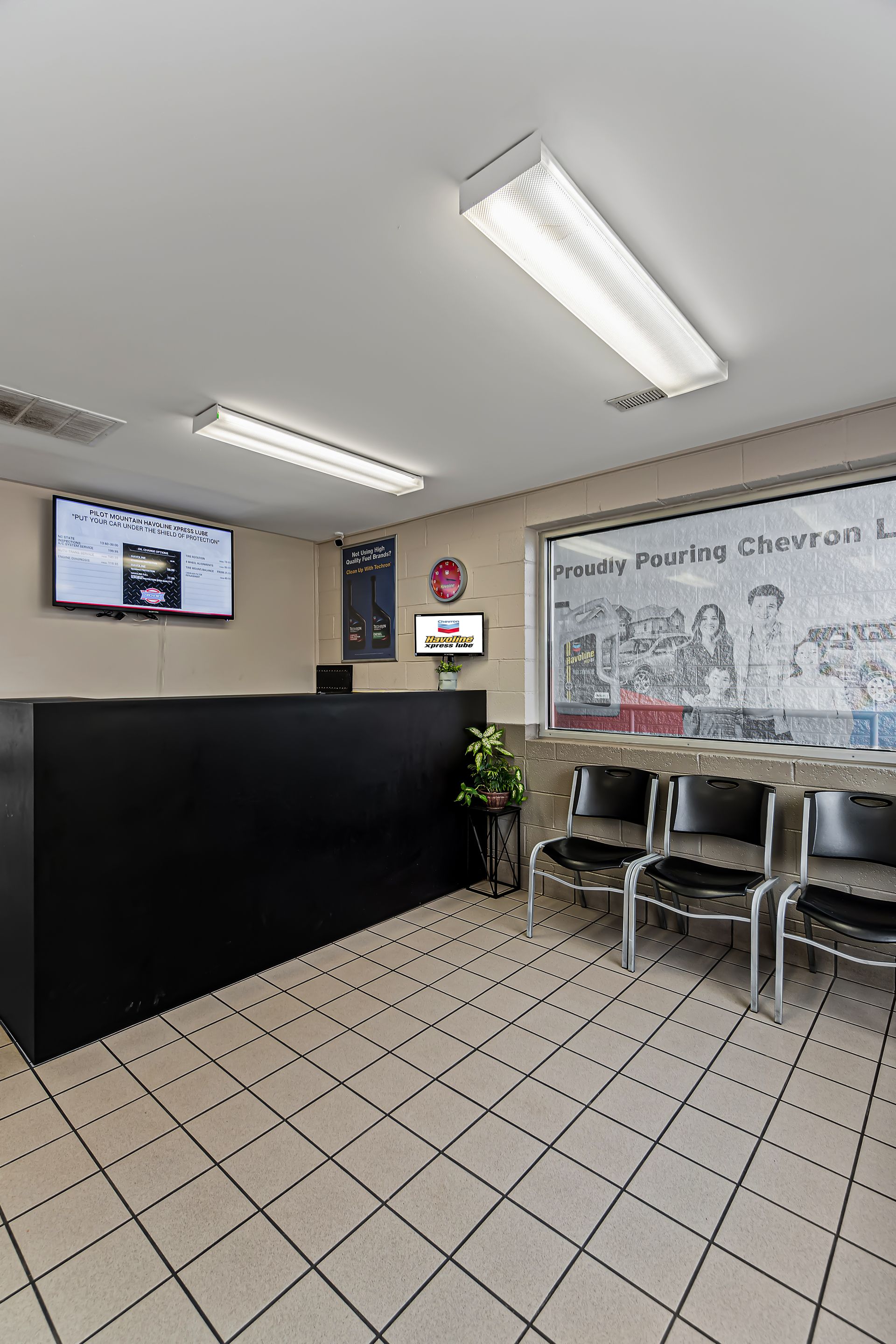 Empty office waiting area with black front desk, wall TV, chairs, whiteboard, and tiled floor.