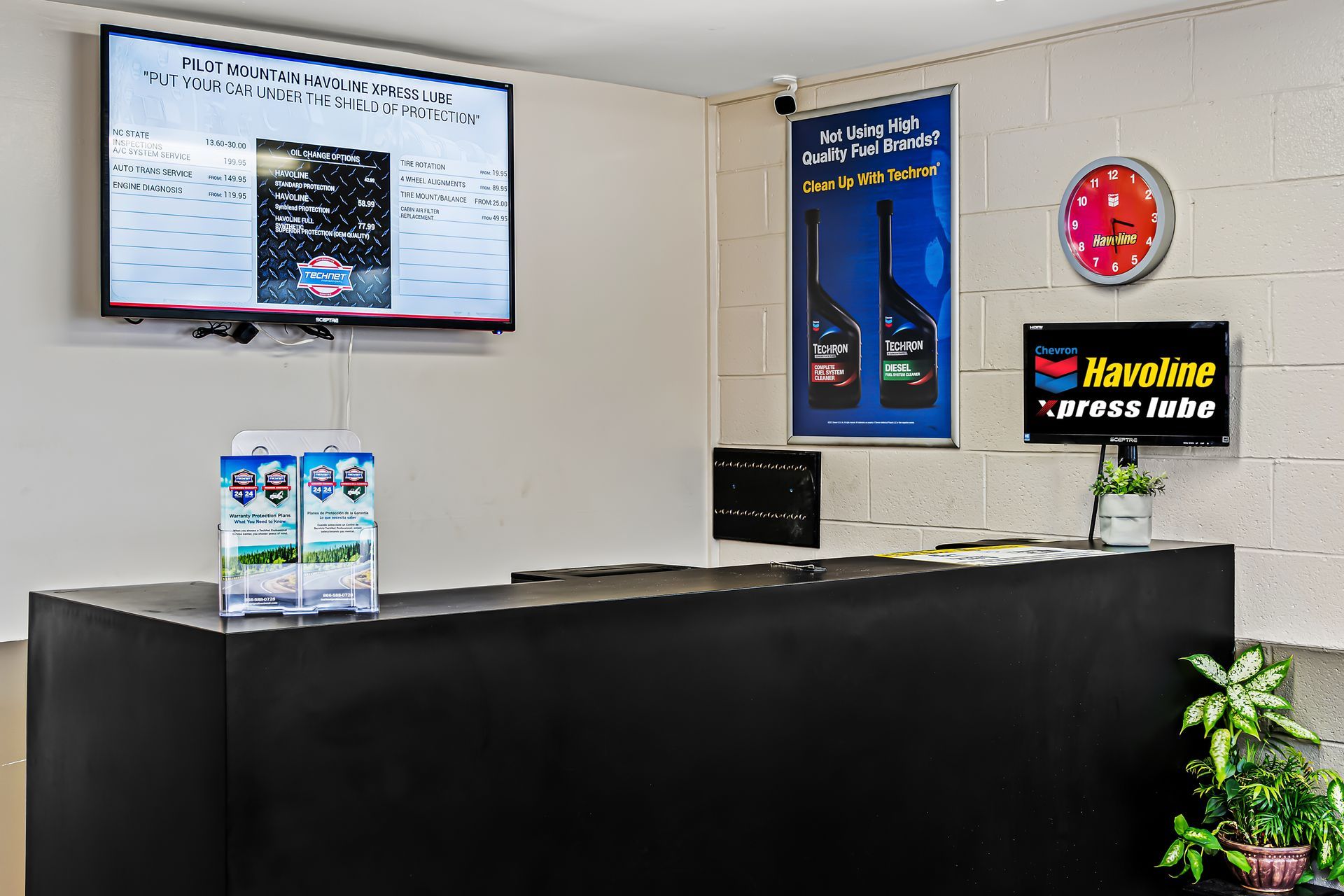 Car rental counter with black desk, wall signs, digital screen, and a plant in the corner