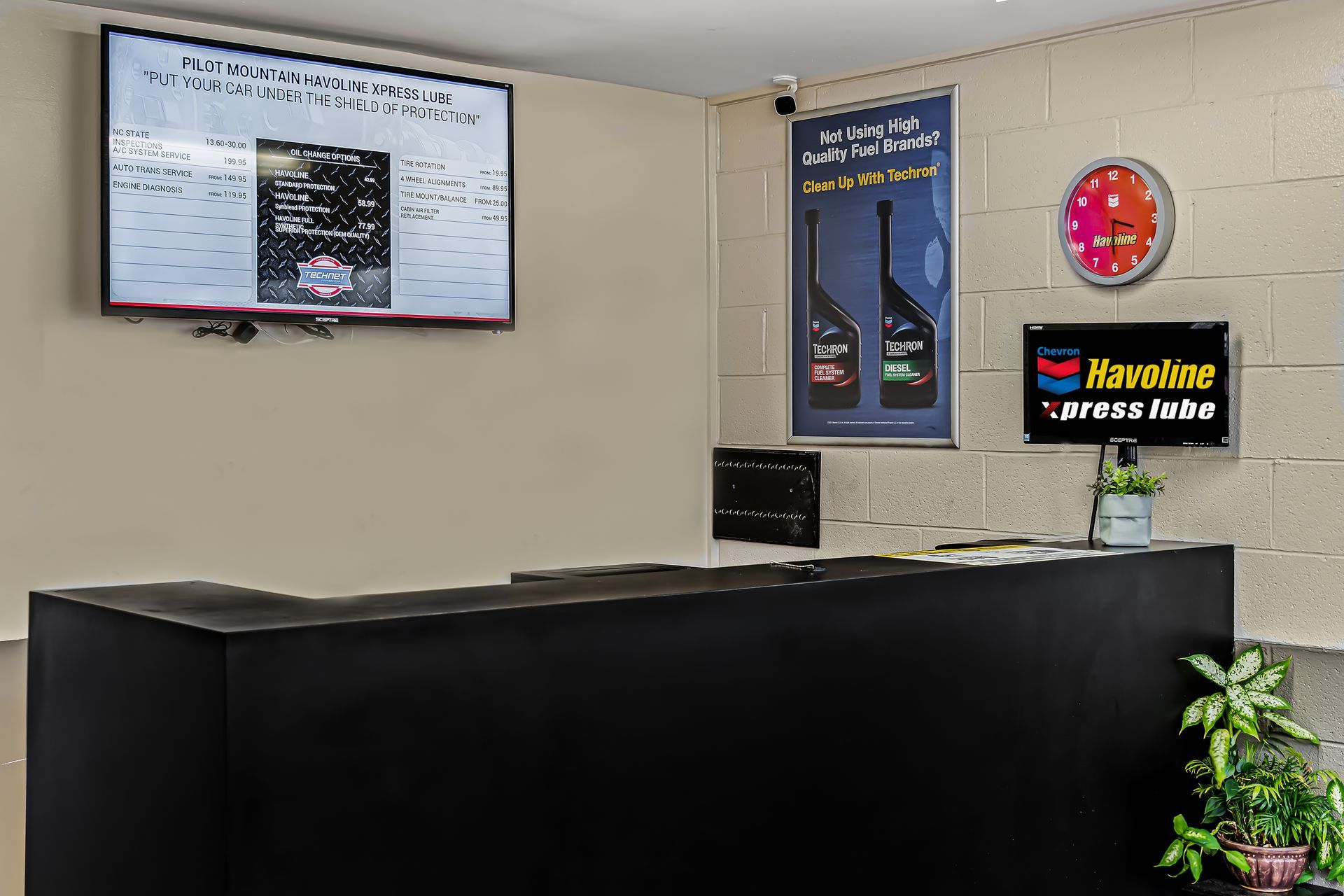 Waiting area with black reception desk, wall-mounted screens, and route signs on a beige wall