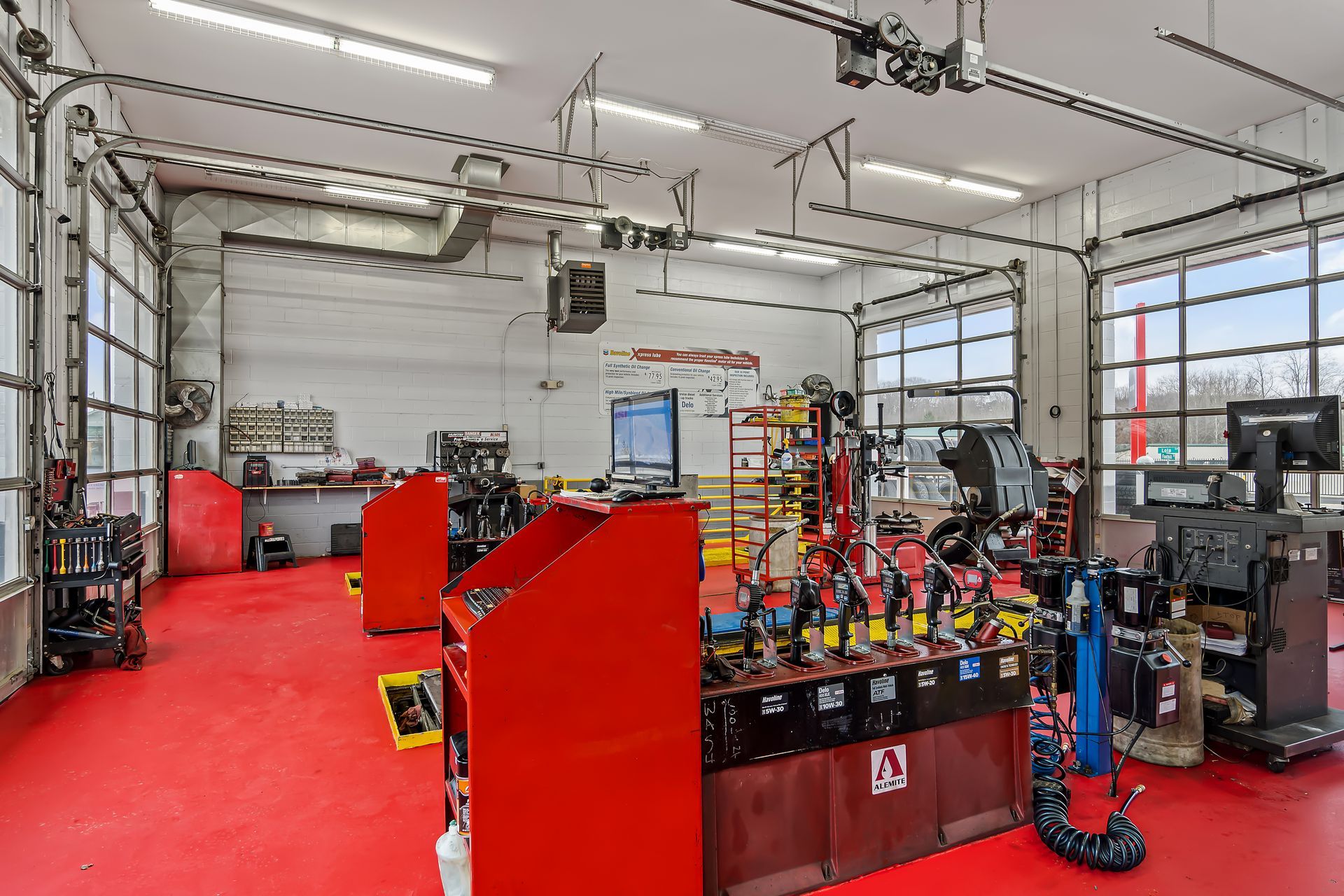 Red-floored workshop with several workbenches, tools, and equipment in a bright garage bay.