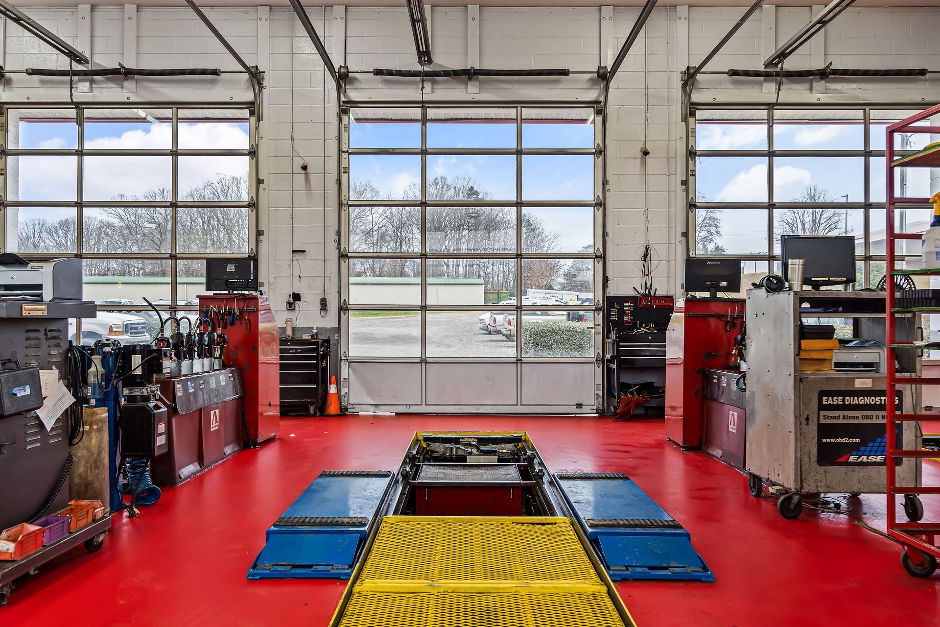 Auto repair shop interior with red floor, vehicle lift, tools, and open garage doors