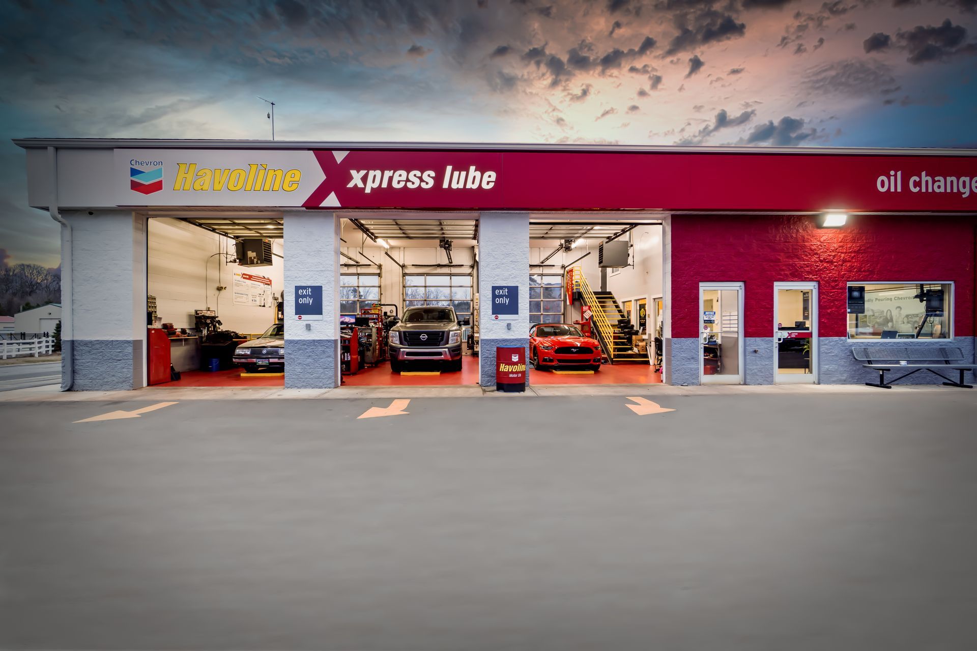 Auto repair shop storefront with open service bays and red signage at dusk
