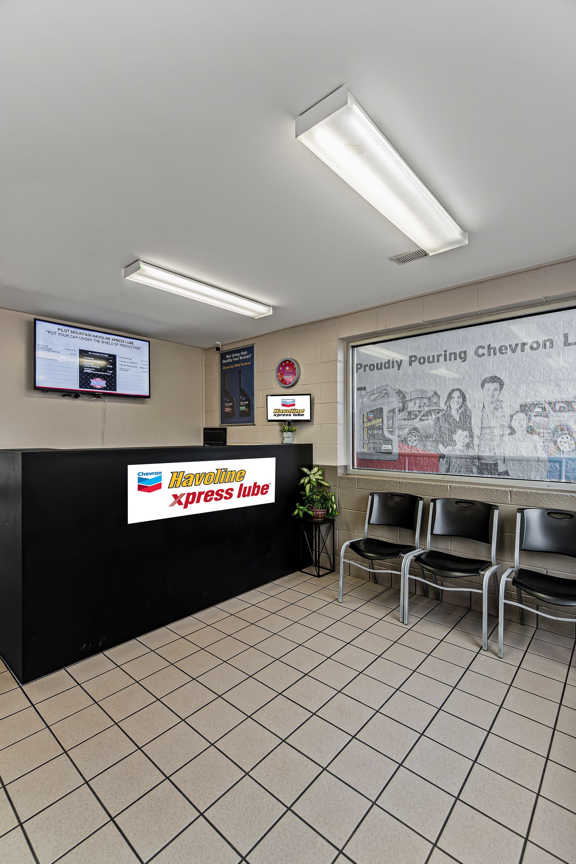 Small office lobby with reception desk, chairs, tiled floor, wall TV, and whiteboard mural.