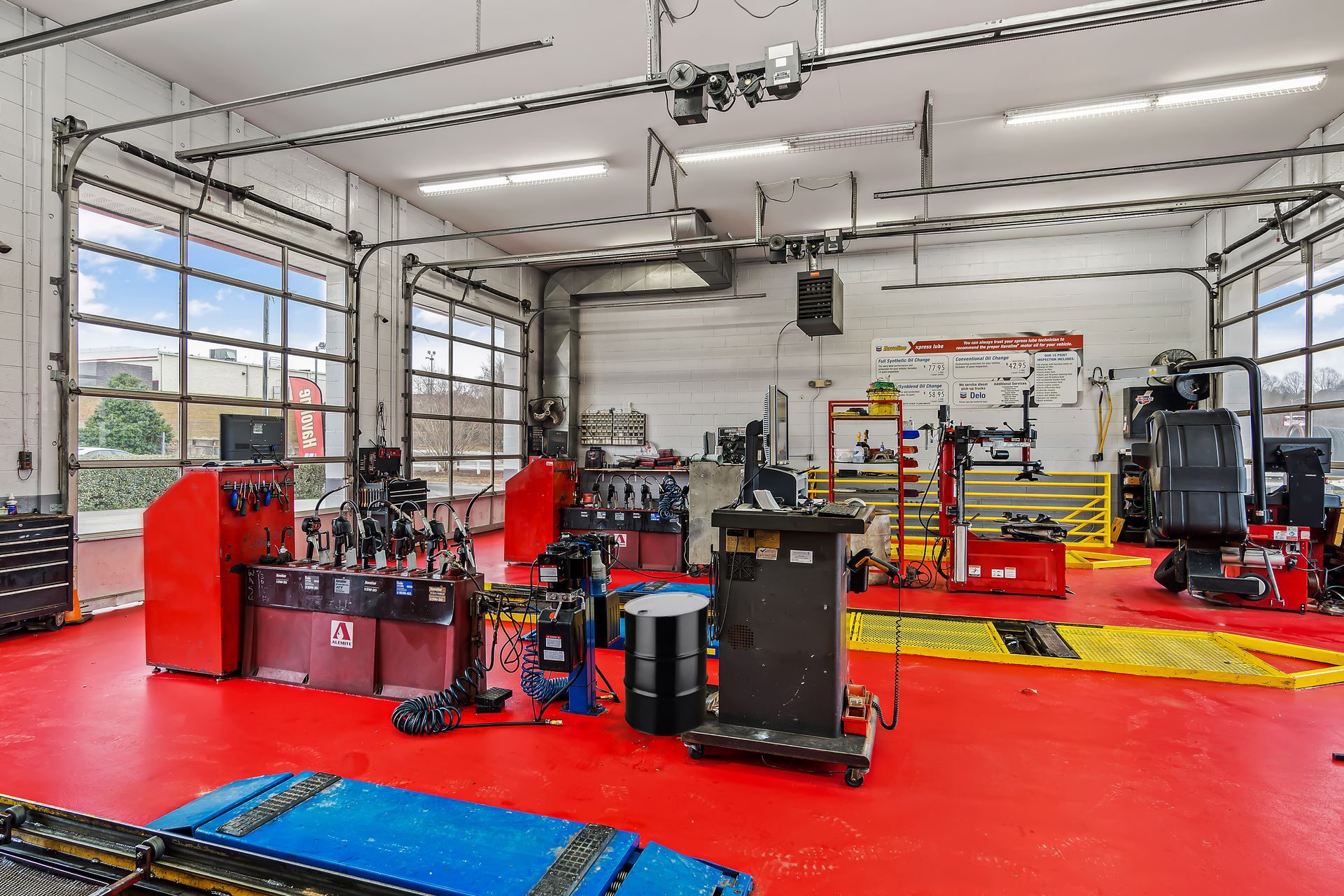 Auto repair shop interior with red floor, vehicle lifts, tools, and equipment in a bright garage