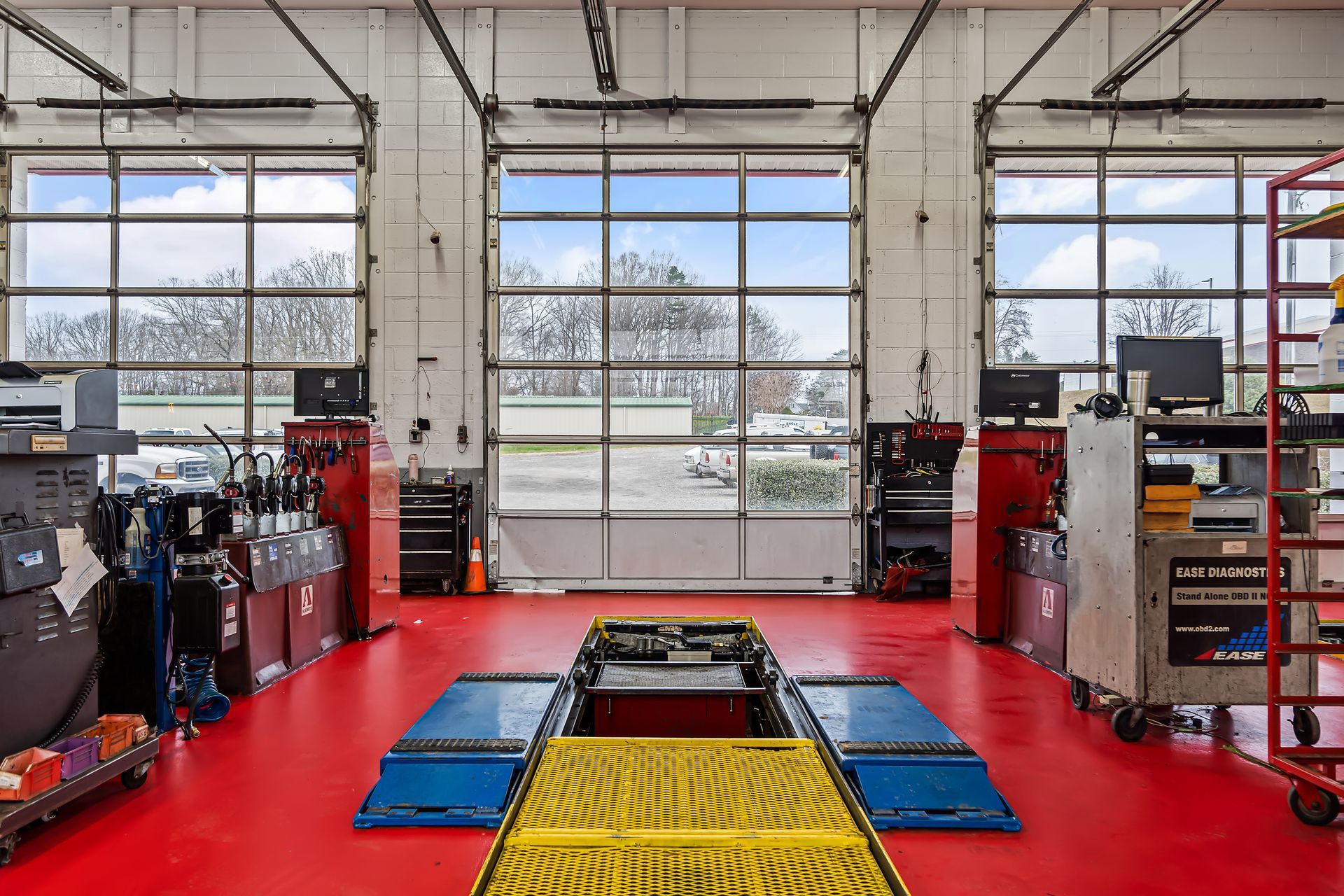 Auto repair shop interior with red floor, blue ramps, and open garage doors