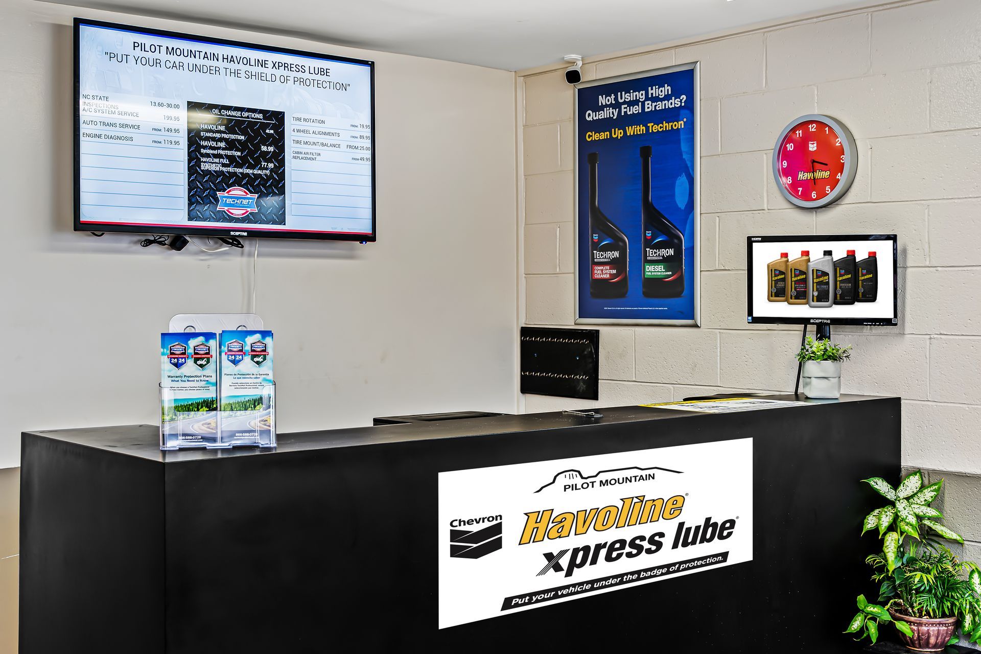 Modern auto service counter with black desk, wall screens, and bright red clock in a clean lobby