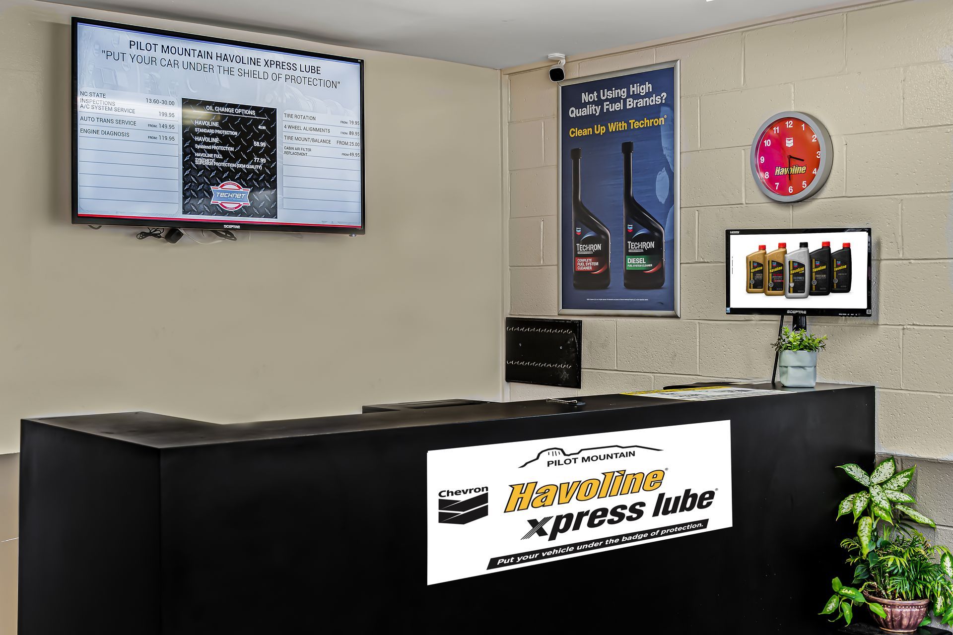 Empty auto service lobby with black counter, wall-mounted menu screens, and red clock.