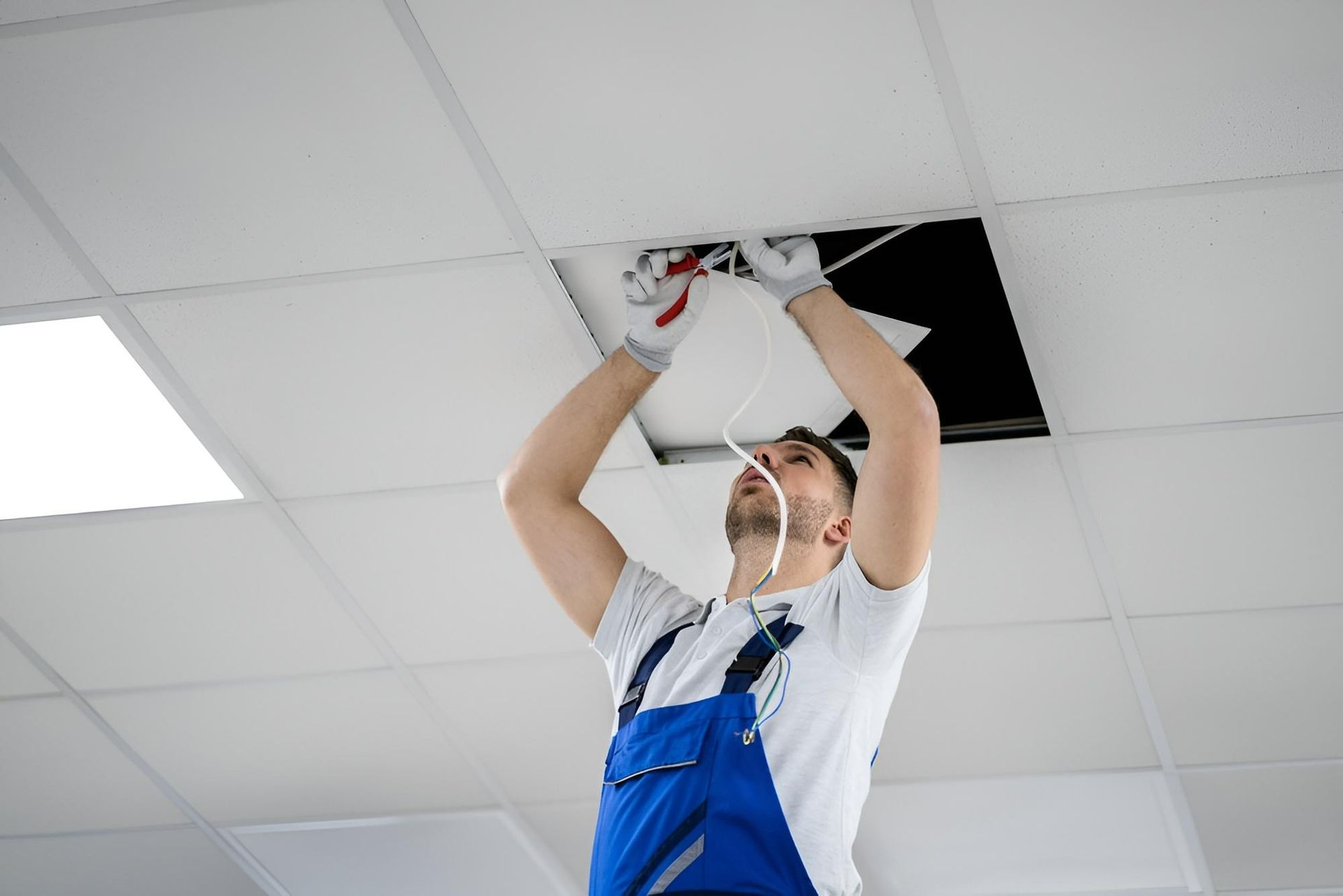 A Man In Blue Overalls Is Working — Chris North Electrical In Jones Hill, QLD
