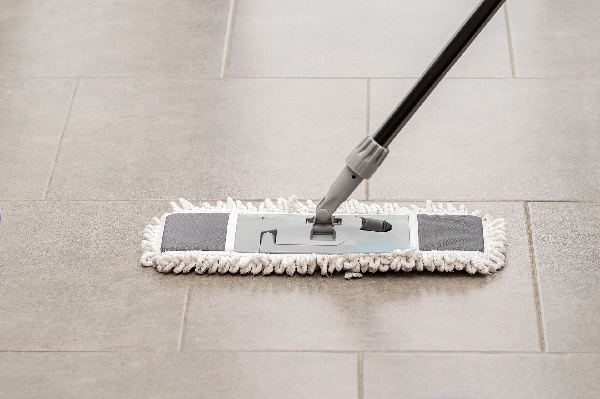 A microfiber dust mop gliding across a large-format gray tile floor with visible grout lines A microfiber dust mop gliding across a large-format gray tile floor with visible grout lines