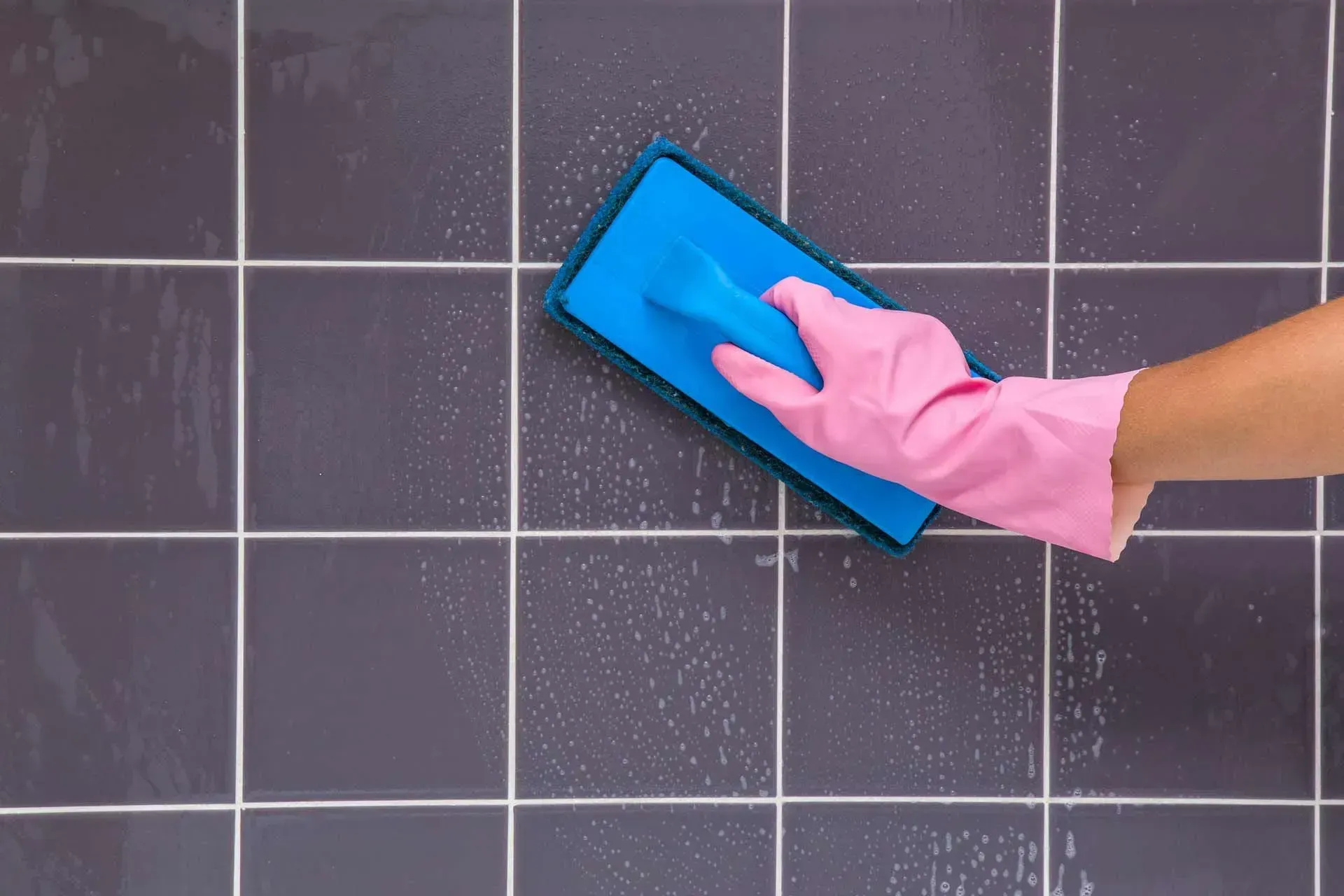 Individual cleaning a tile surface with a sponge, highlighting tile cleaning services in Hancock Par