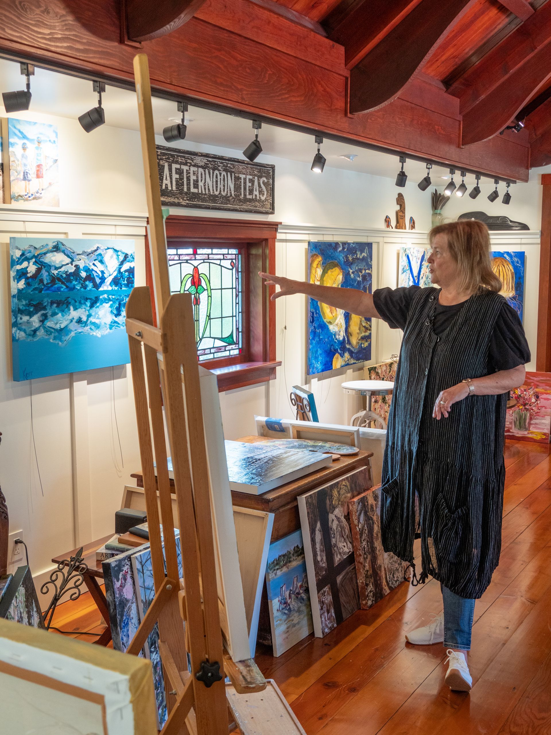 Hilary standing in front of her art, pointing at a piece hanging on the wall. 