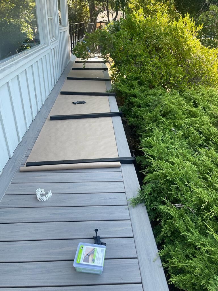 Deck with rolled-up paper and tools, alongside a green hedge, next to a building with windows.