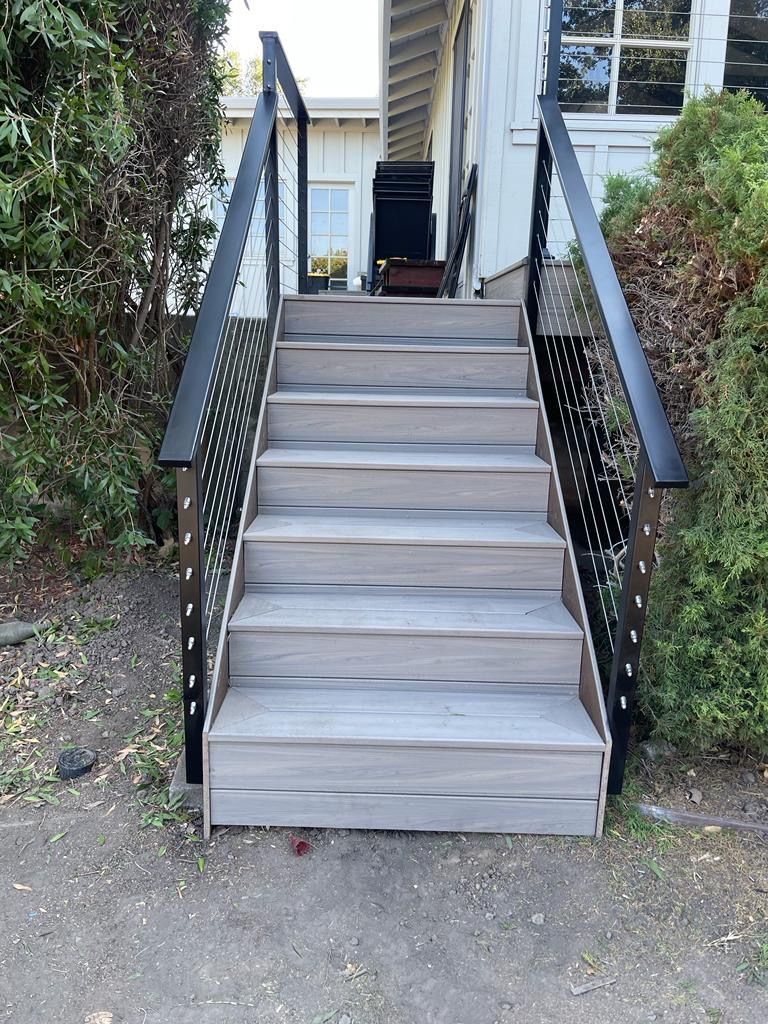 Wooden outdoor stairs with black metal railings leading to a white building's entrance.