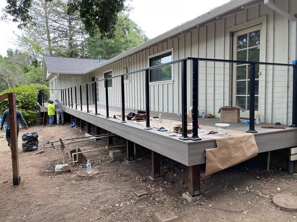 A deck is under construction with a black railing, next to a white house with workers present.