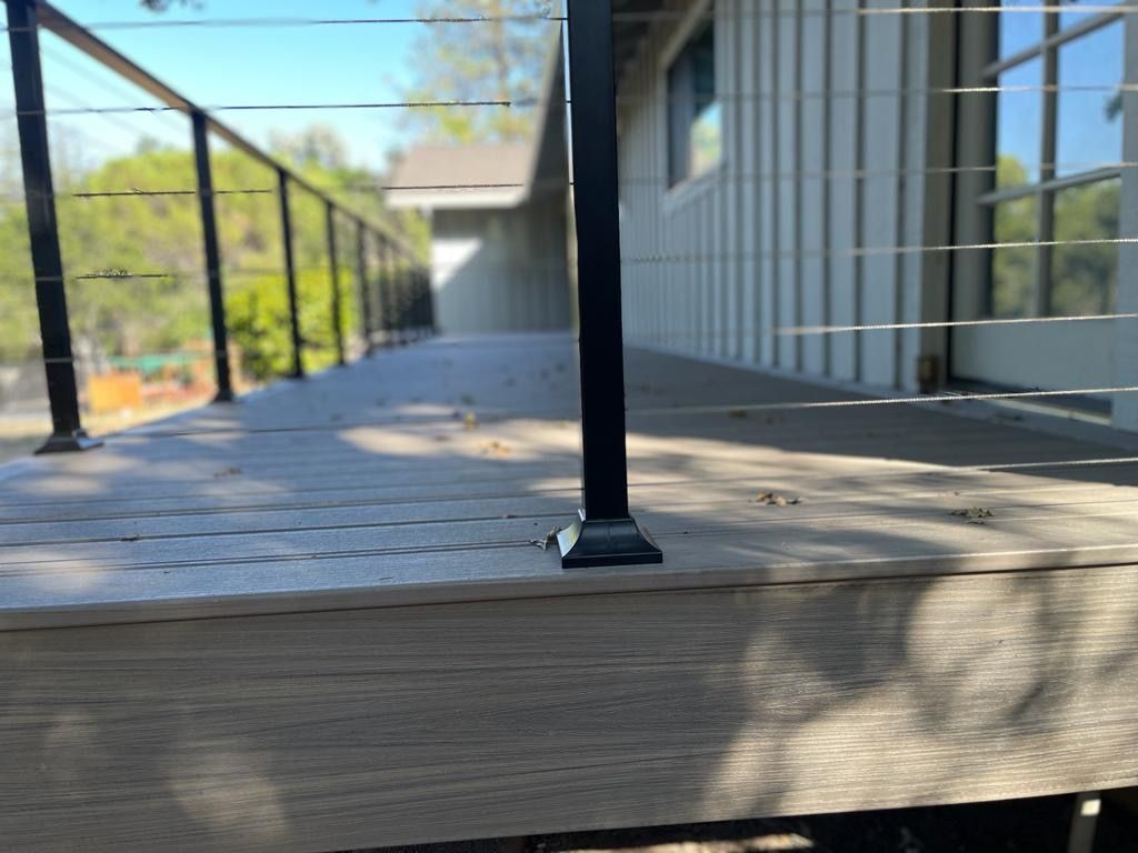 Deck with metal railing and cable infill next to a white house.