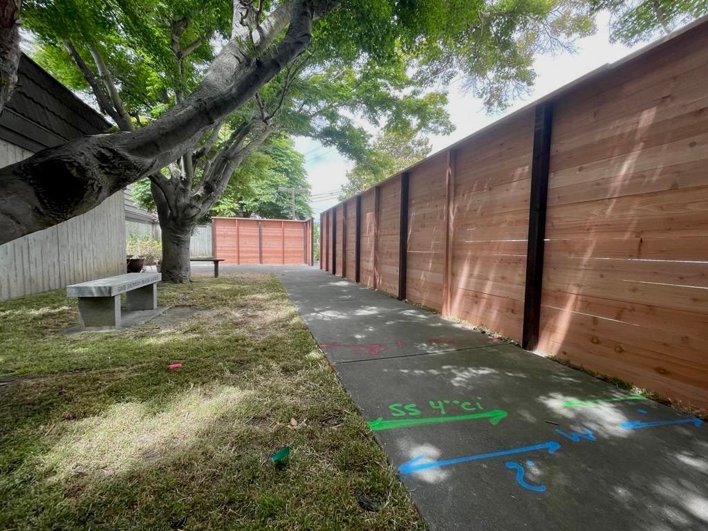 A paved walkway with painted arrows and a wooden fence, tree, bench, and building.