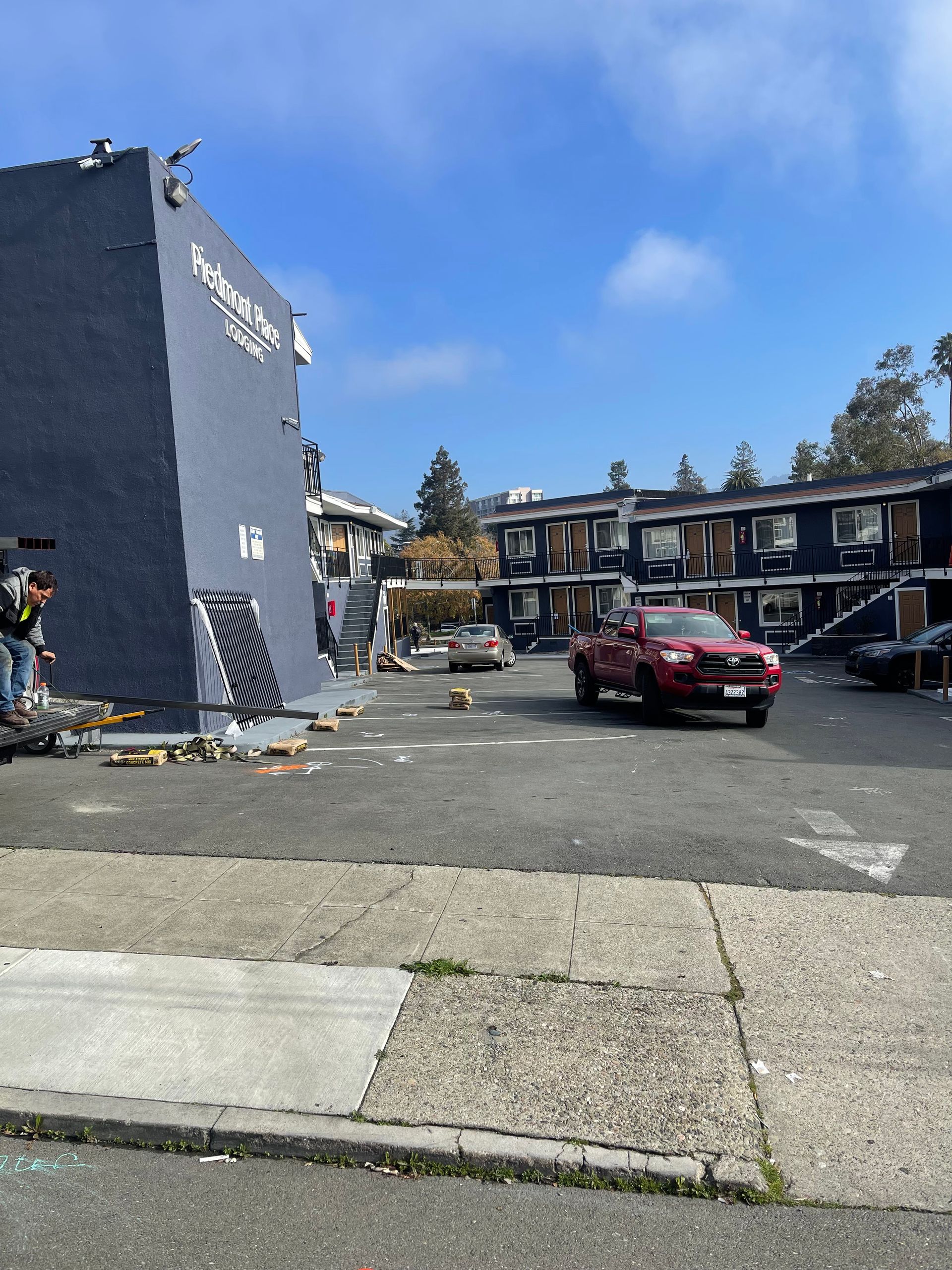 A dark blue apartment building with a red truck driving through a parking lot on a sunny day.