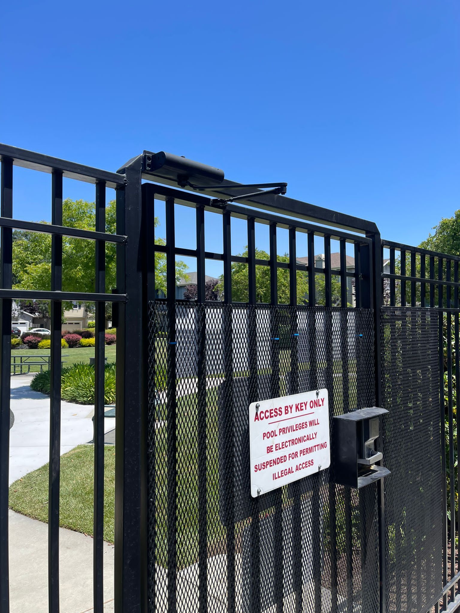 Black metal gate with sign, outdoors under blue sky.
