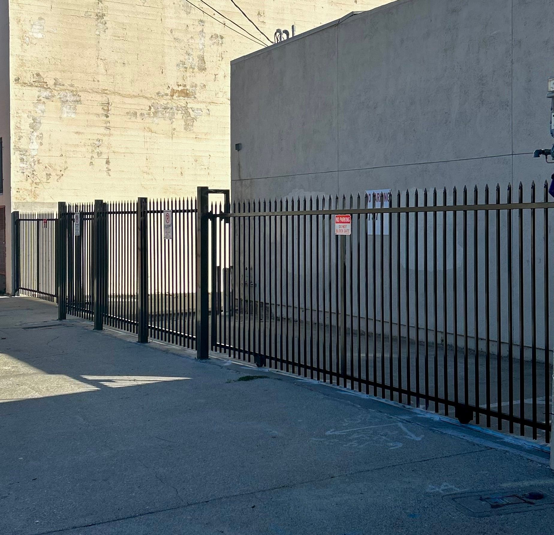 Black metal fence along a concrete walkway, next to a pale building.