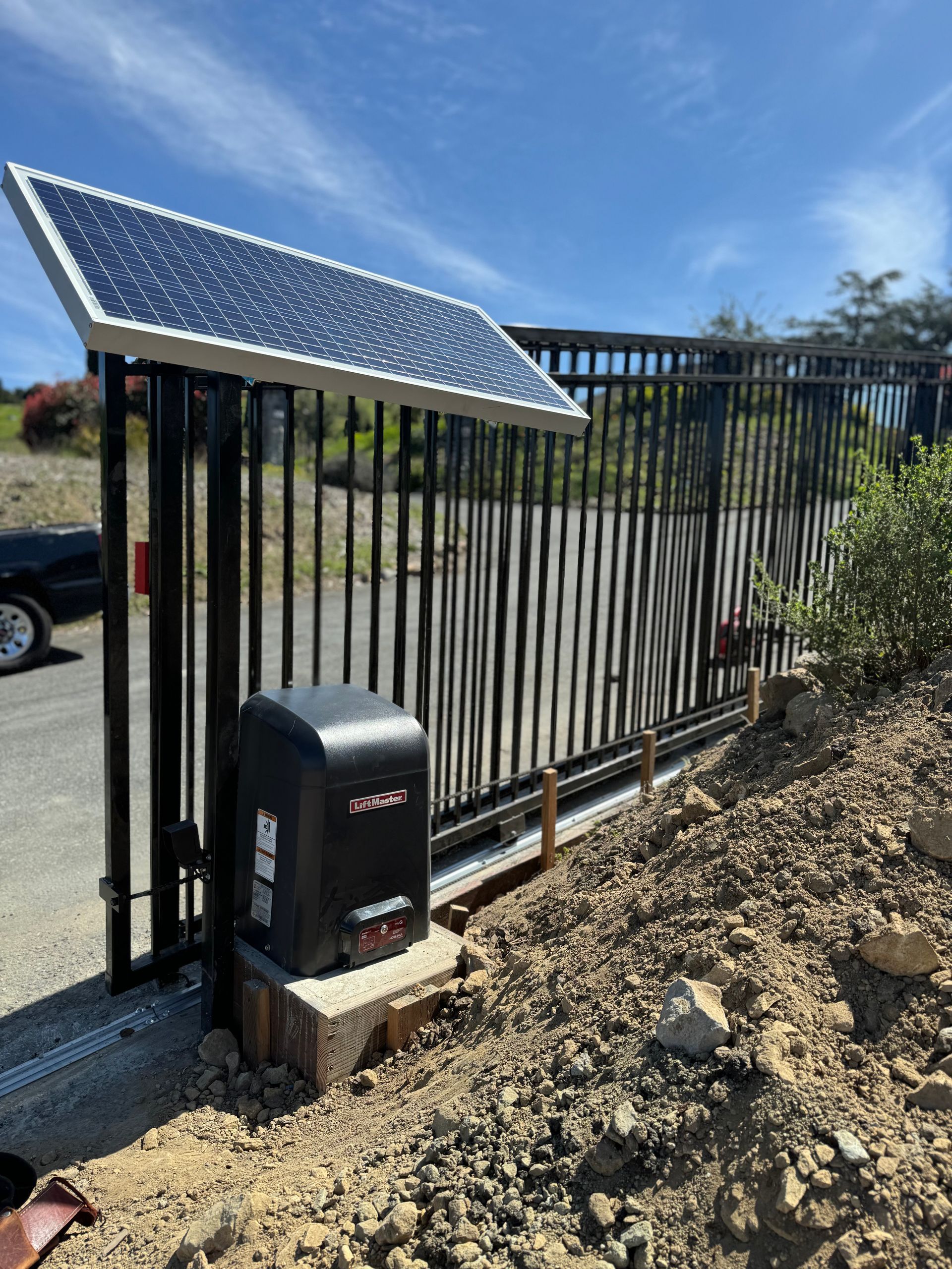 Solar-powered black metal gate beside a gravel path and driveway.