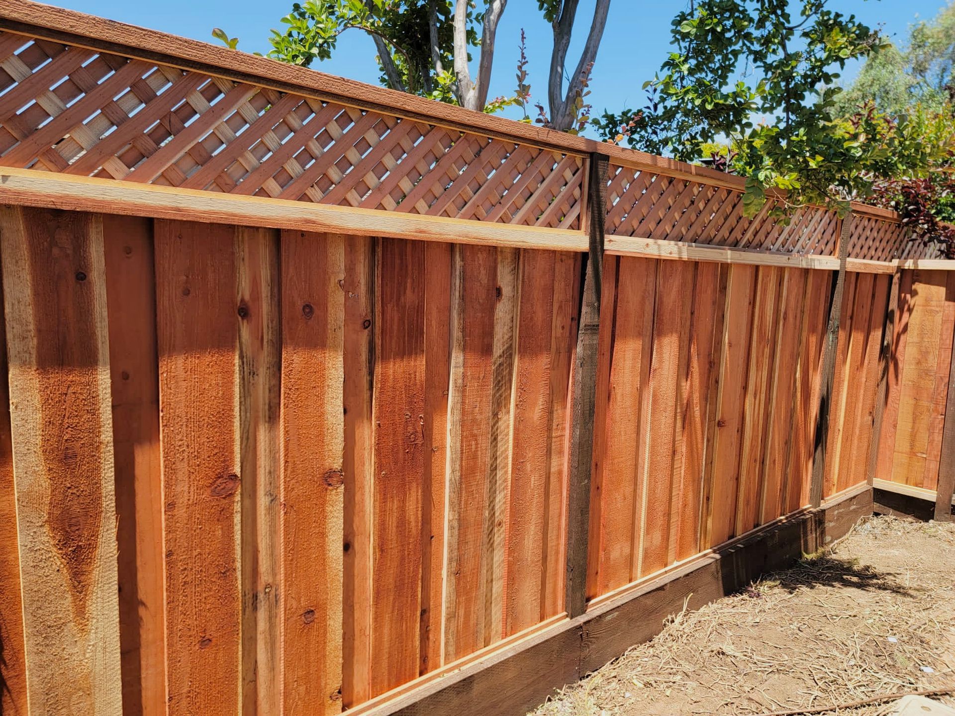 Wooden fence with lattice top, stained in a reddish-brown color, set in a yard.