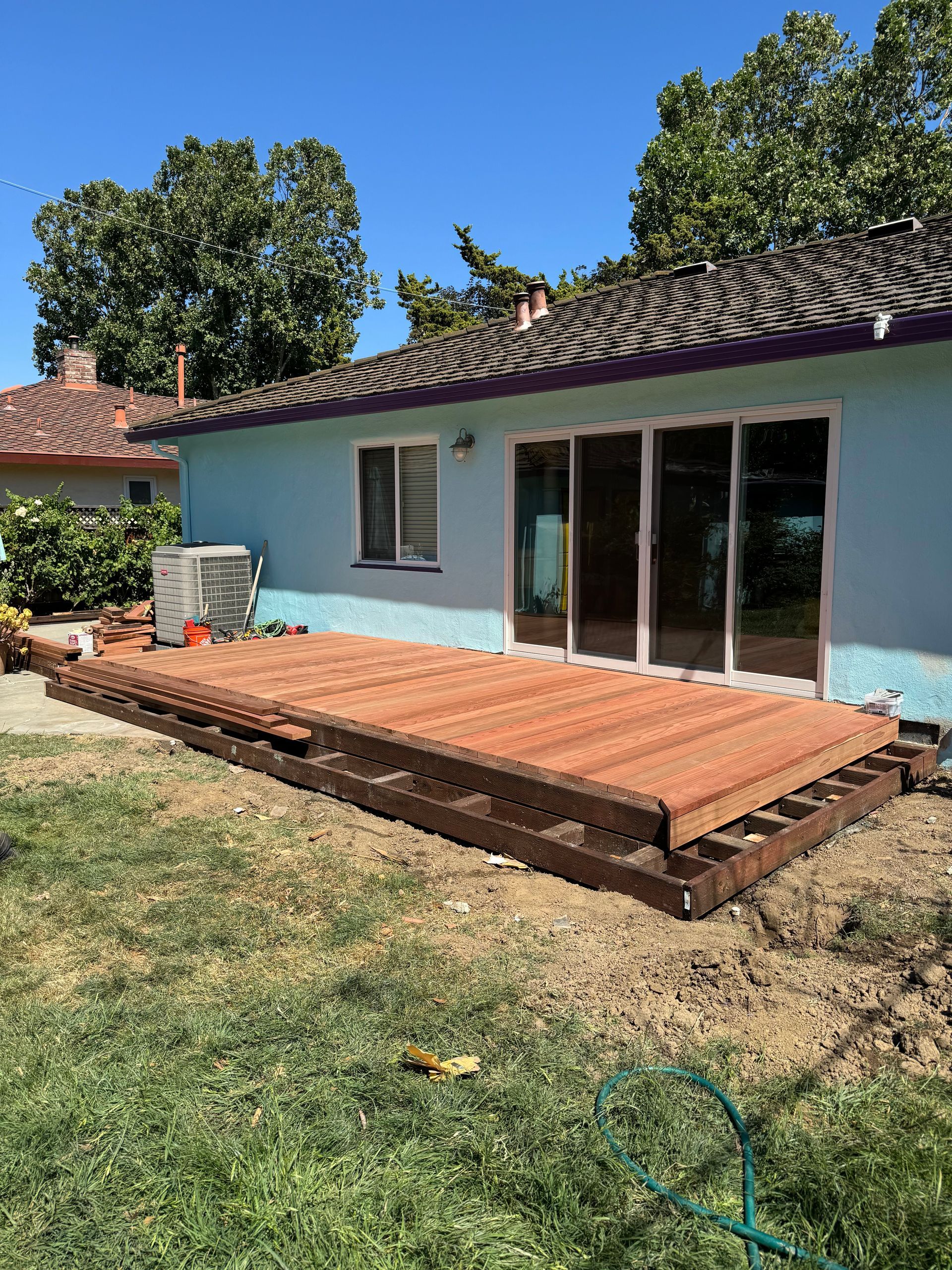 Partially built brown wooden deck outside a blue house with sliding glass doors.