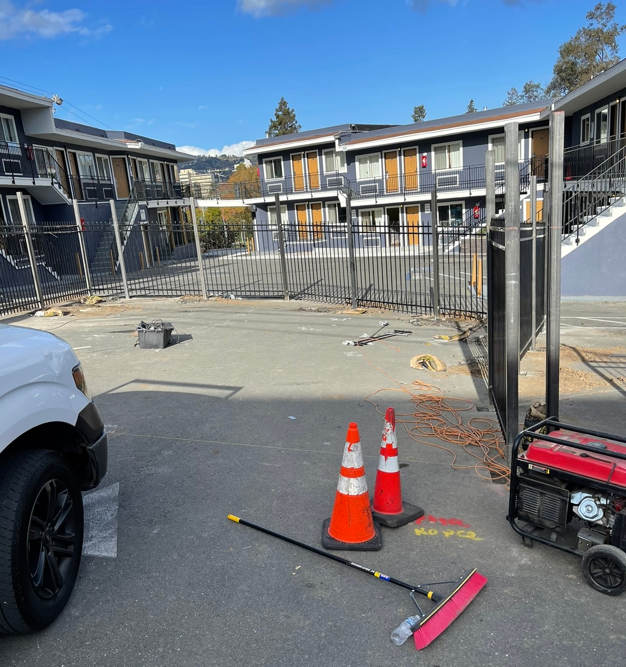 Construction zone with orange cones, a generator, and a work vehicle. Buildings in the background.