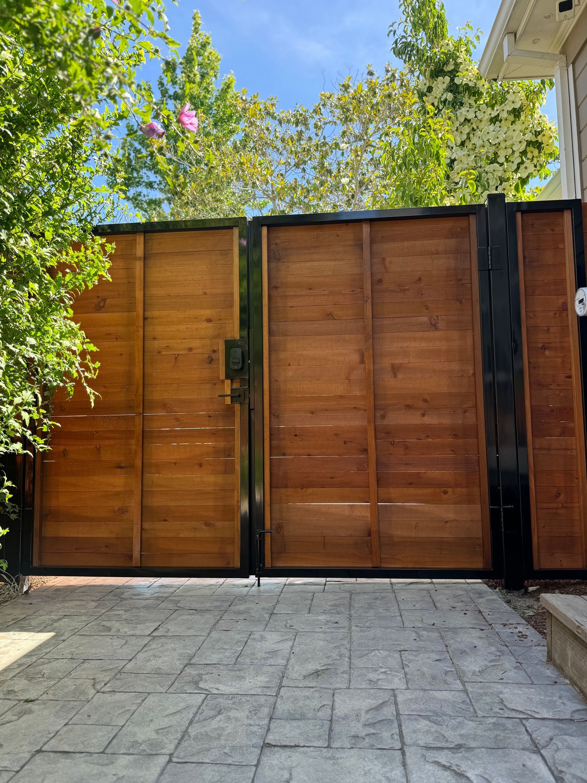 A double wooden gate with a black metal frame stands at the end of a paved stone path.