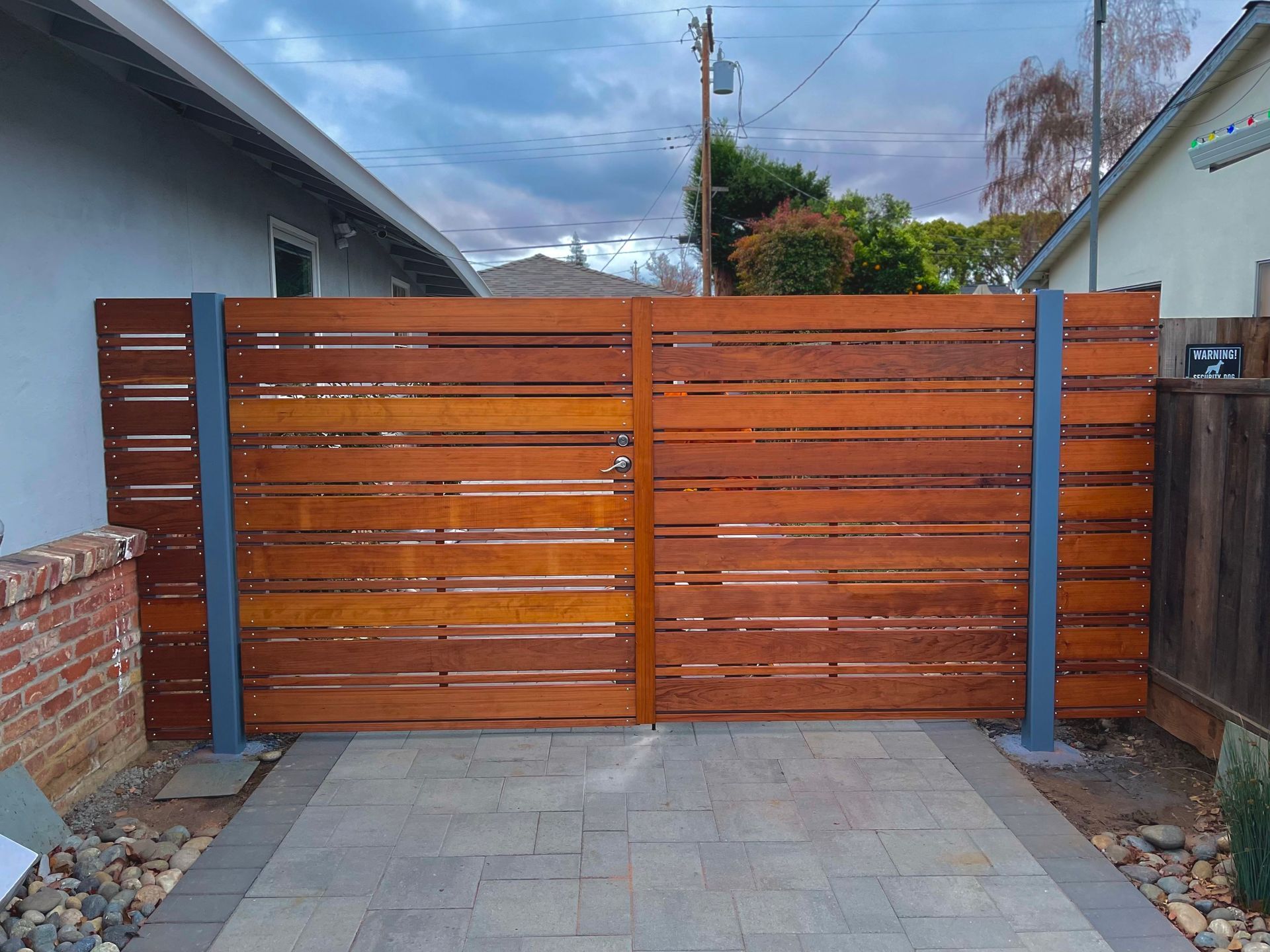 Wooden gate with horizontal slats, framed by gray metal posts, set in a paved driveway.
