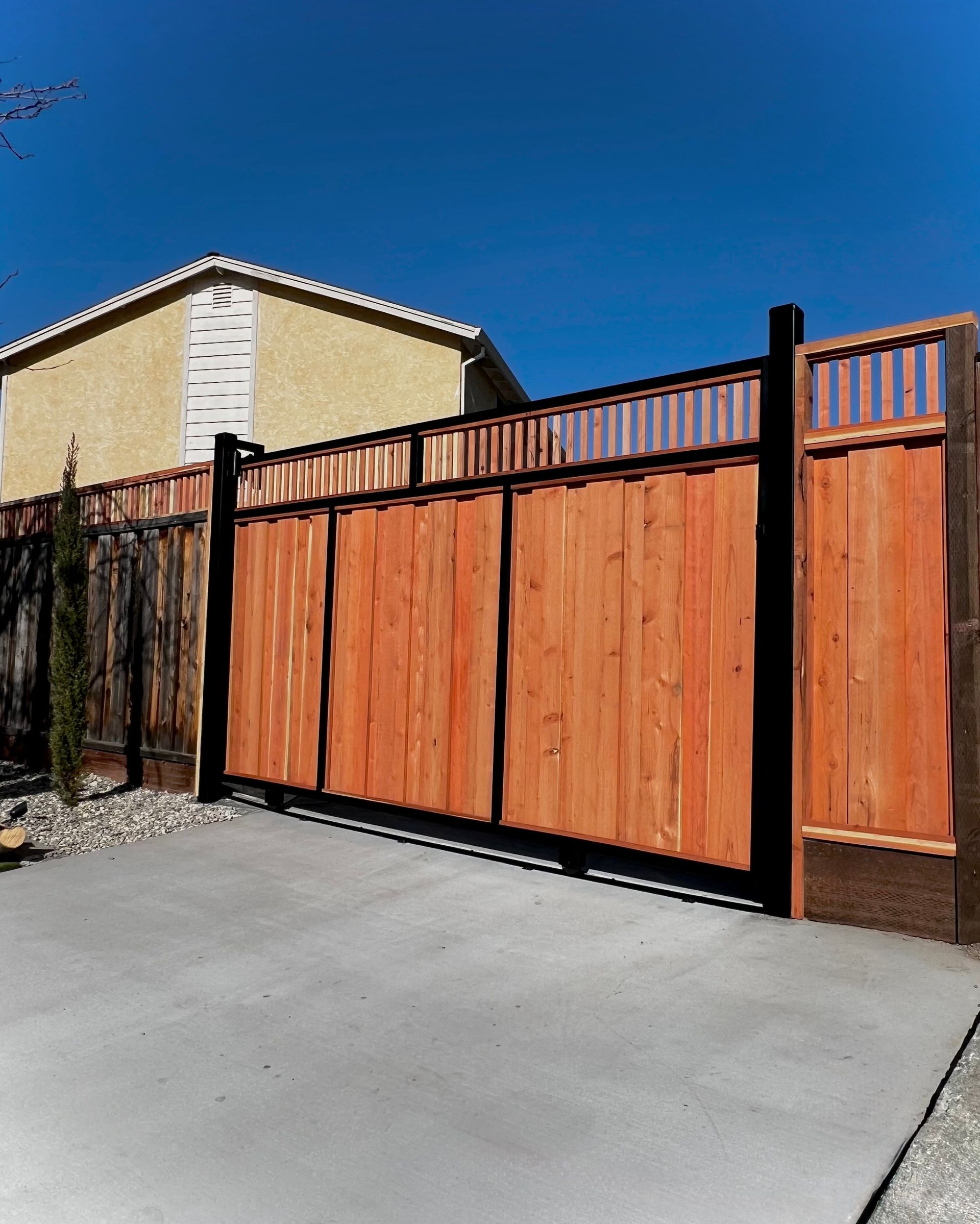 Wooden privacy fence and gate beside a driveway under a clear blue sky