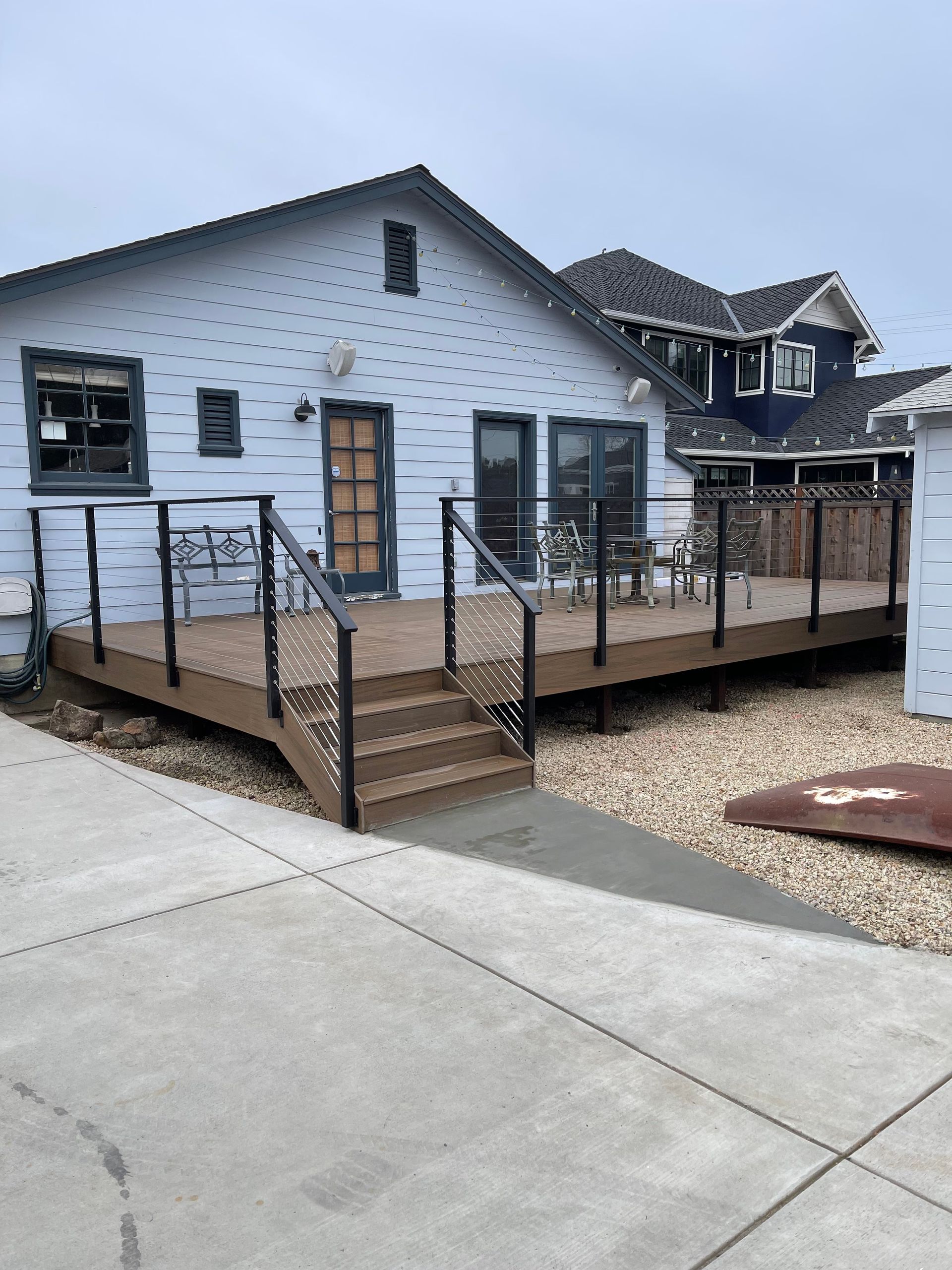 A wooden deck with a black metal railing and horizontal cable infill, located alongside a house exterior.