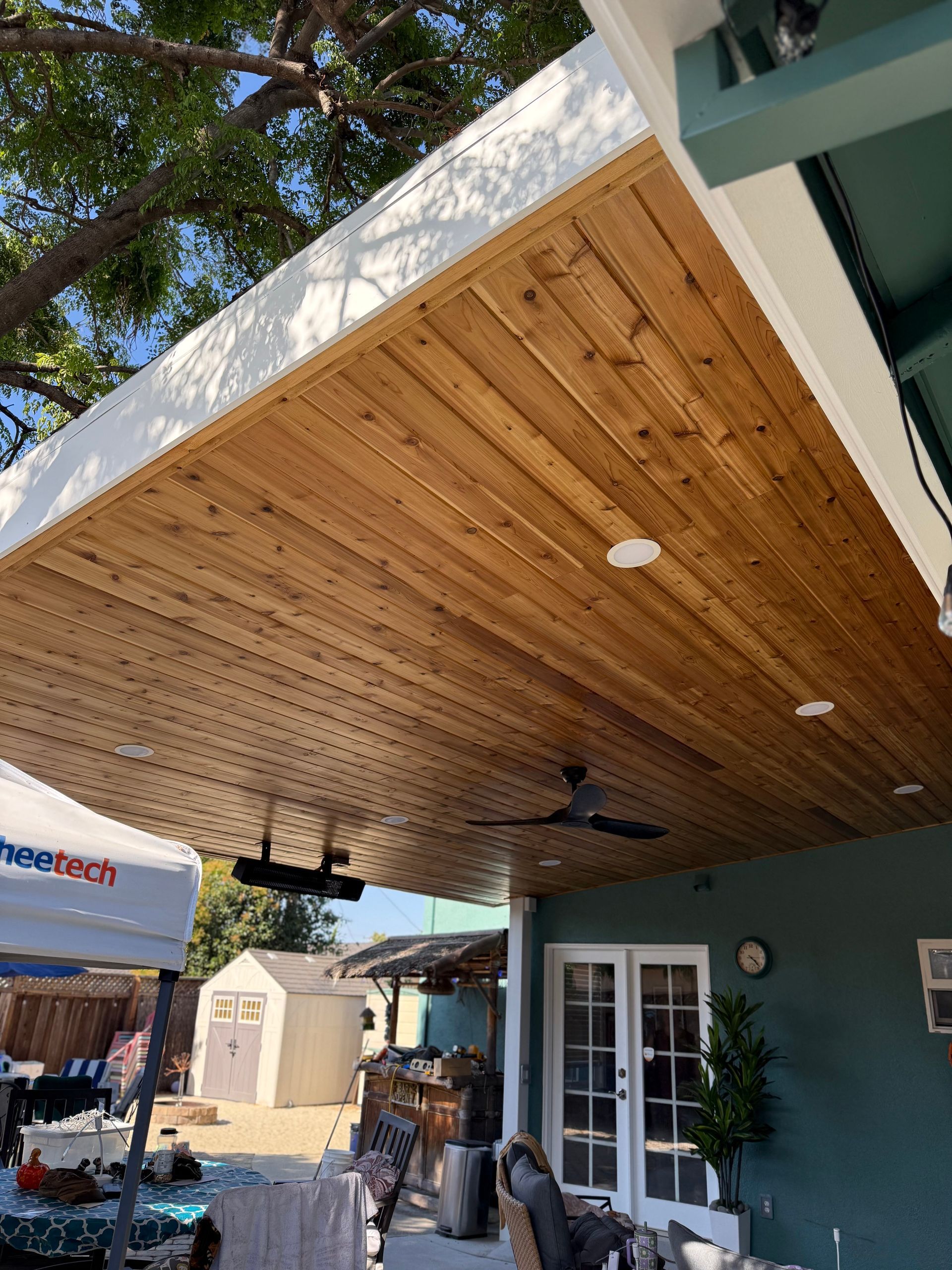 Covered patio with wood ceiling, ceiling fans, and French doors beside a green house
